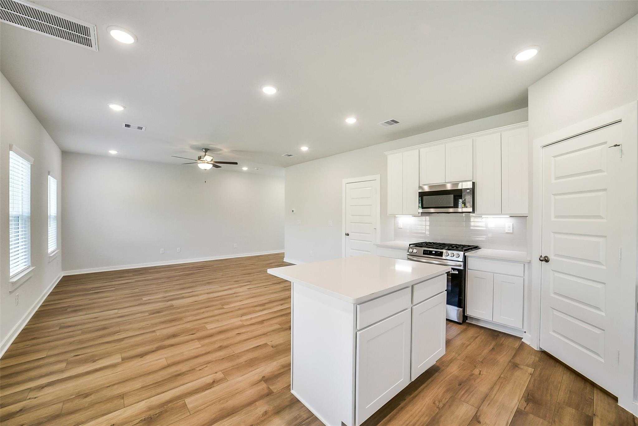 Modern open-concept kitchen with white quartz island, stainless appliances, and hardwood floors in Davidson Homes The Trinity F, Magnolia, Texas