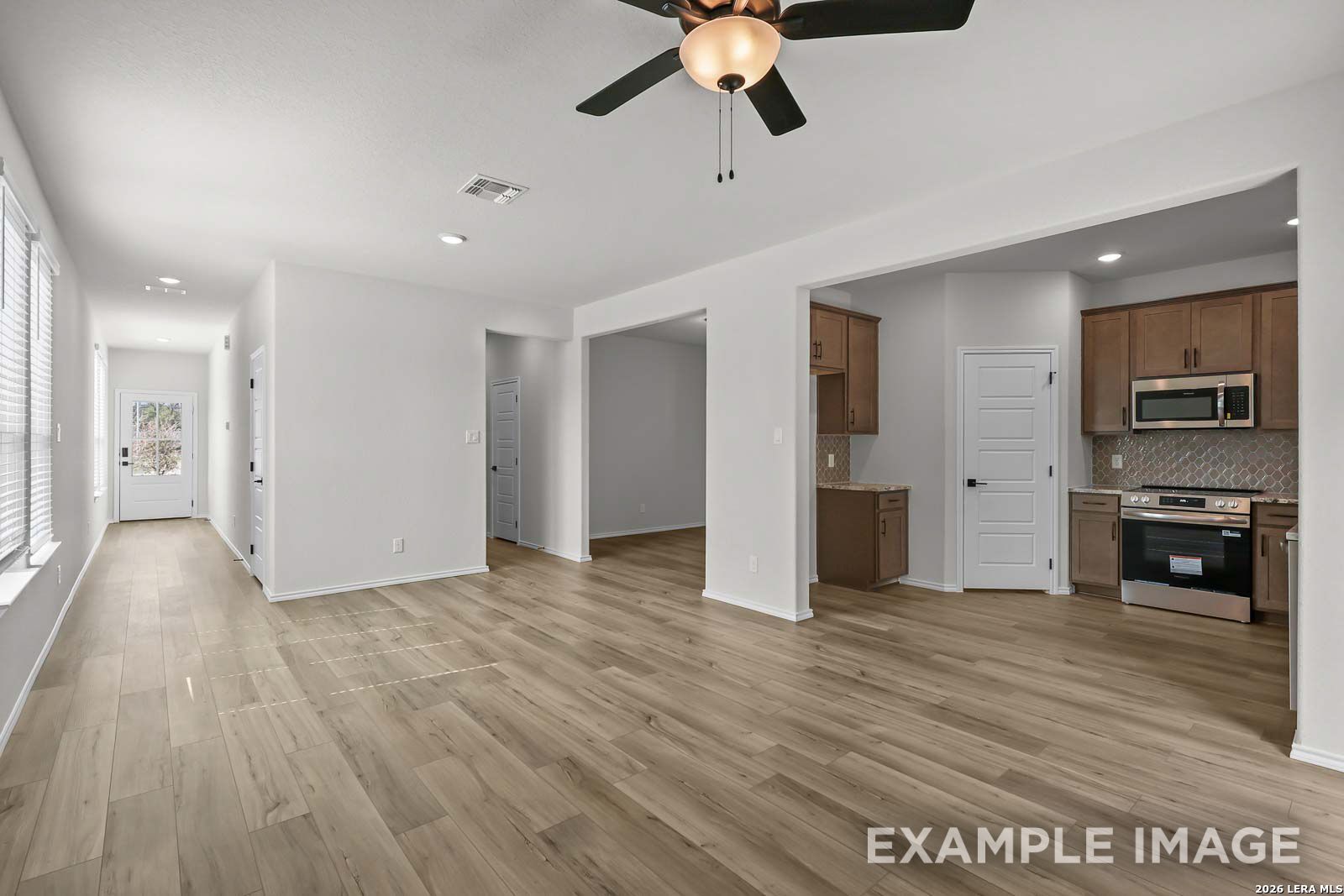 Open-concept living area with wood-look flooring and kitchen view in The Florence D floor plan, Cedar Heights, San Antonio.