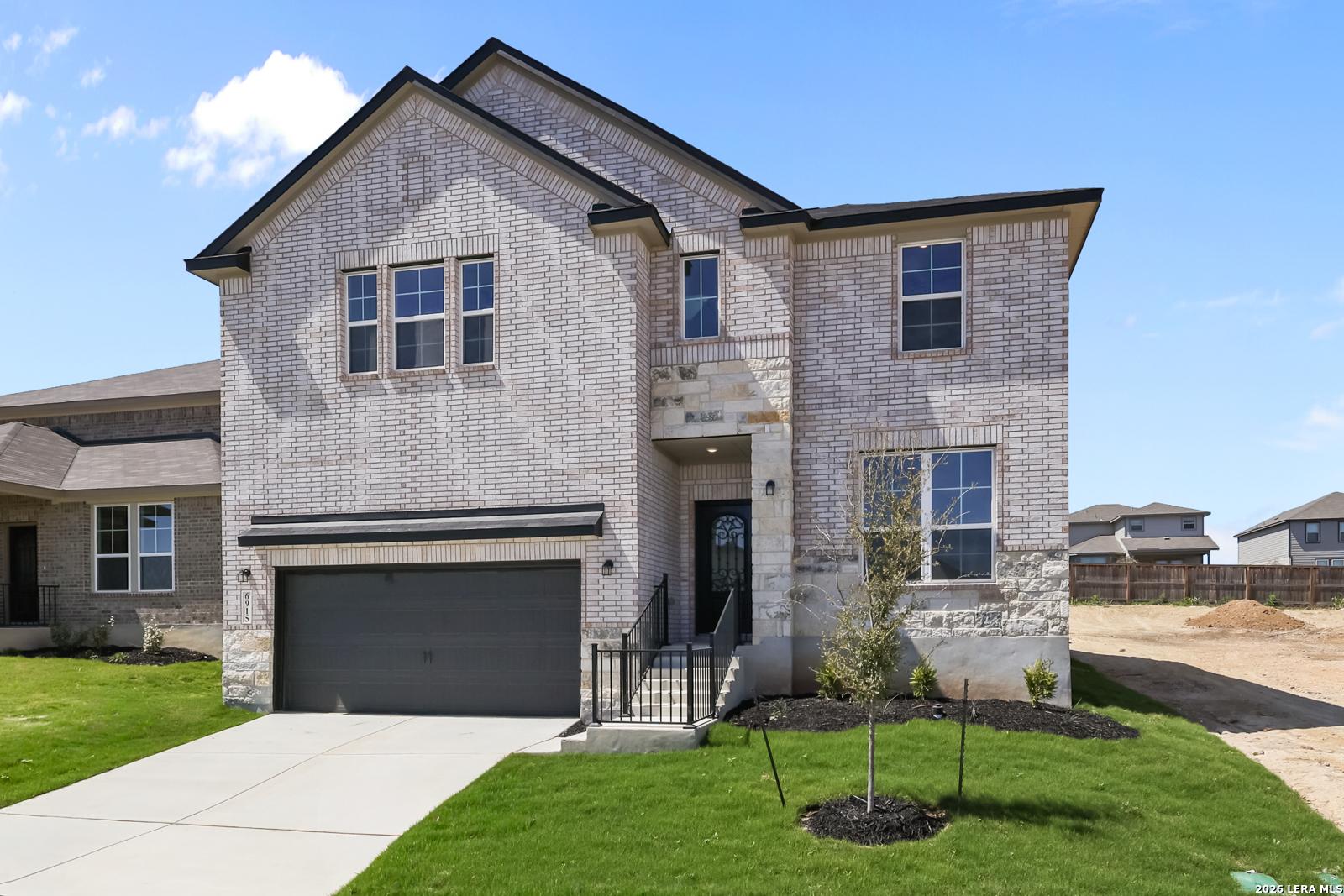 Light brick two-story home with two-car garage, covered entry, and front yard landscaping in Comanche Ridge, San Antonio, Texas - Davidson Homes Sequoia B