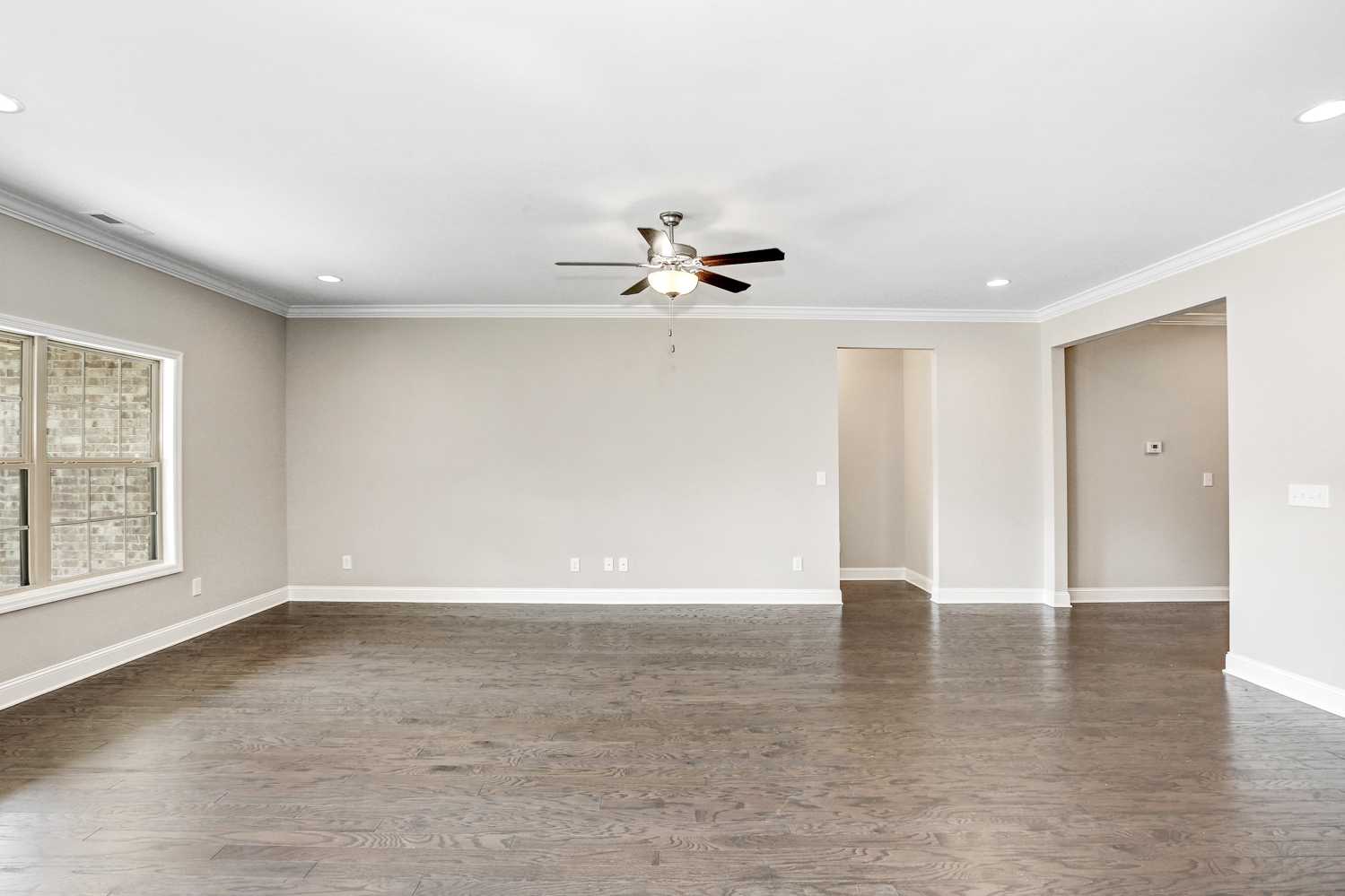 Spacious living room in The Montgomery home featuring beige walls, hardwood floors, ceiling fan, and large window views