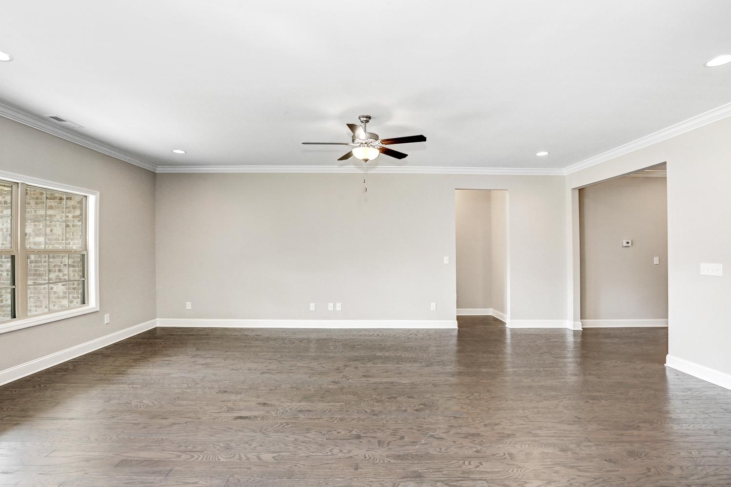Spacious living room in The Montgomery home featuring beige walls, hardwood floors, ceiling fan, and large window views