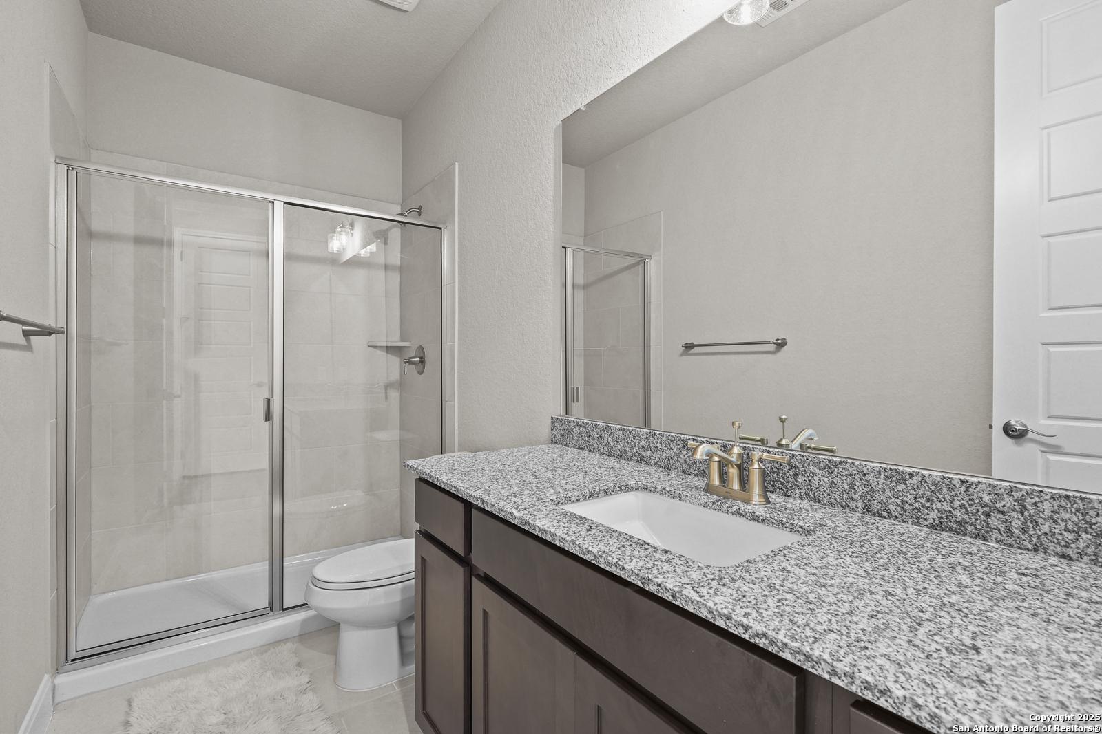 Modern guest bathroom featuring granite vanity, glass shower enclosure, and neutral tile in Davidson Homes The Jennings G, Castroville, Texas