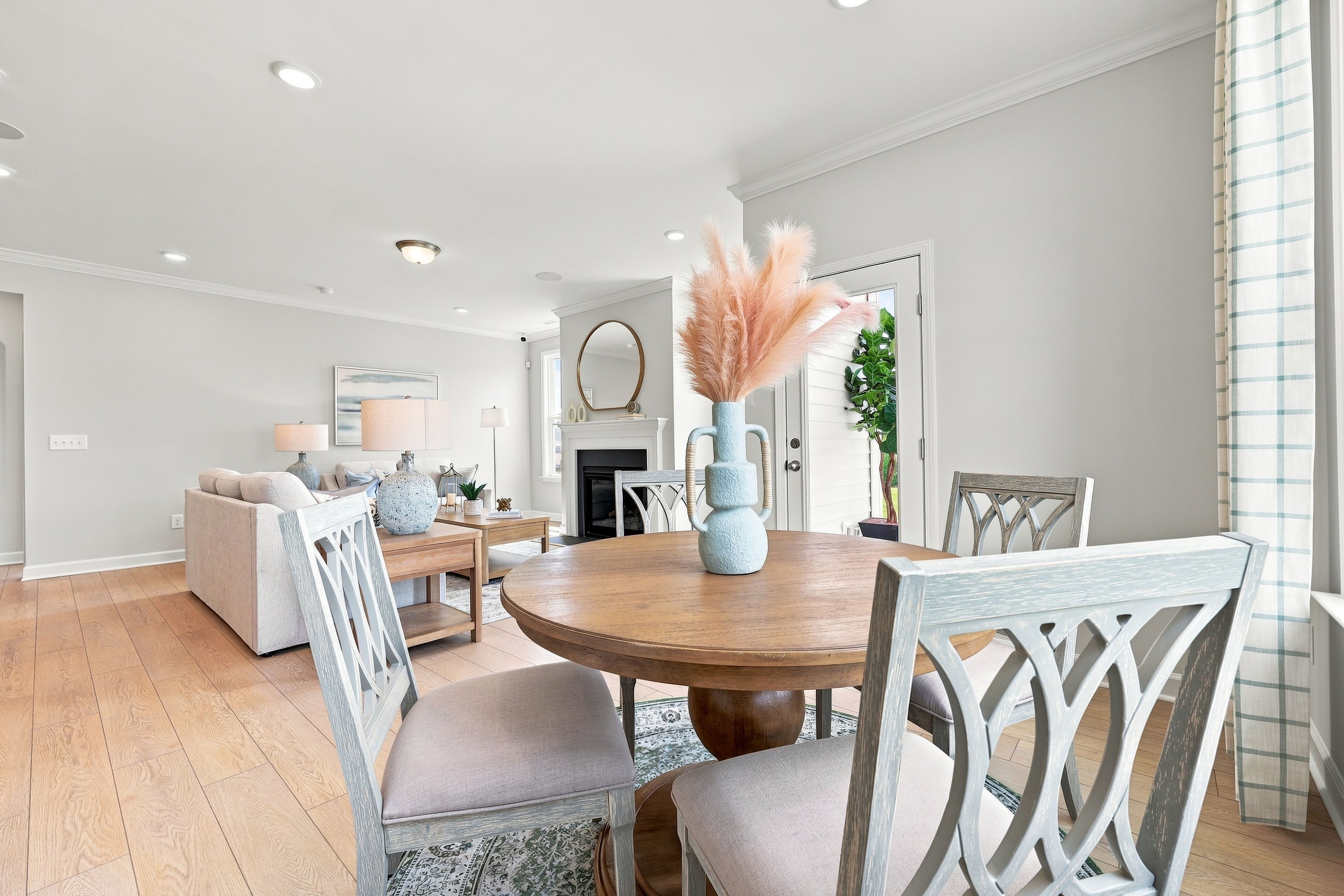Open-concept living and dining area in The Daphne D featuring a round wooden table, light-filled space, and fireplace.