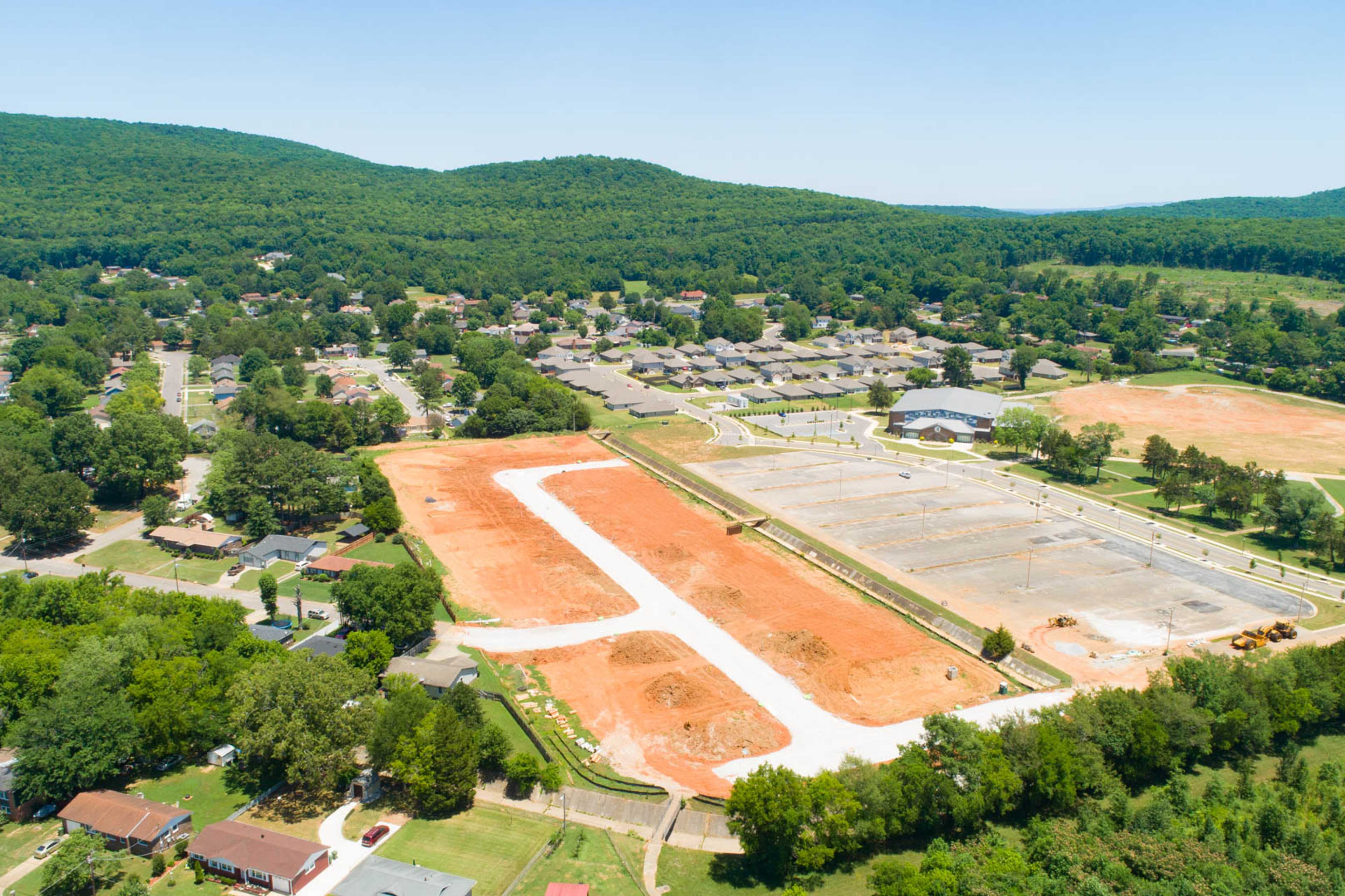 Aerial view of Jaguar Hills construction in Huntsville AL with red dirt lots, sports fields, parking areas, and wooded hills