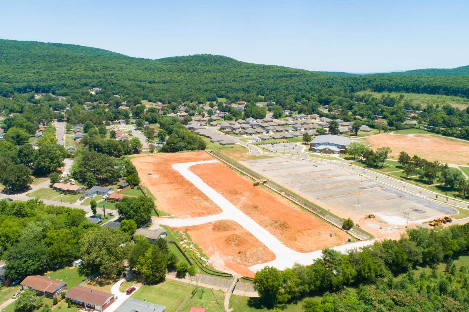 Aerial view of Jaguar Hills construction in Huntsville AL with red dirt lots, sports fields, parking areas, and wooded hills