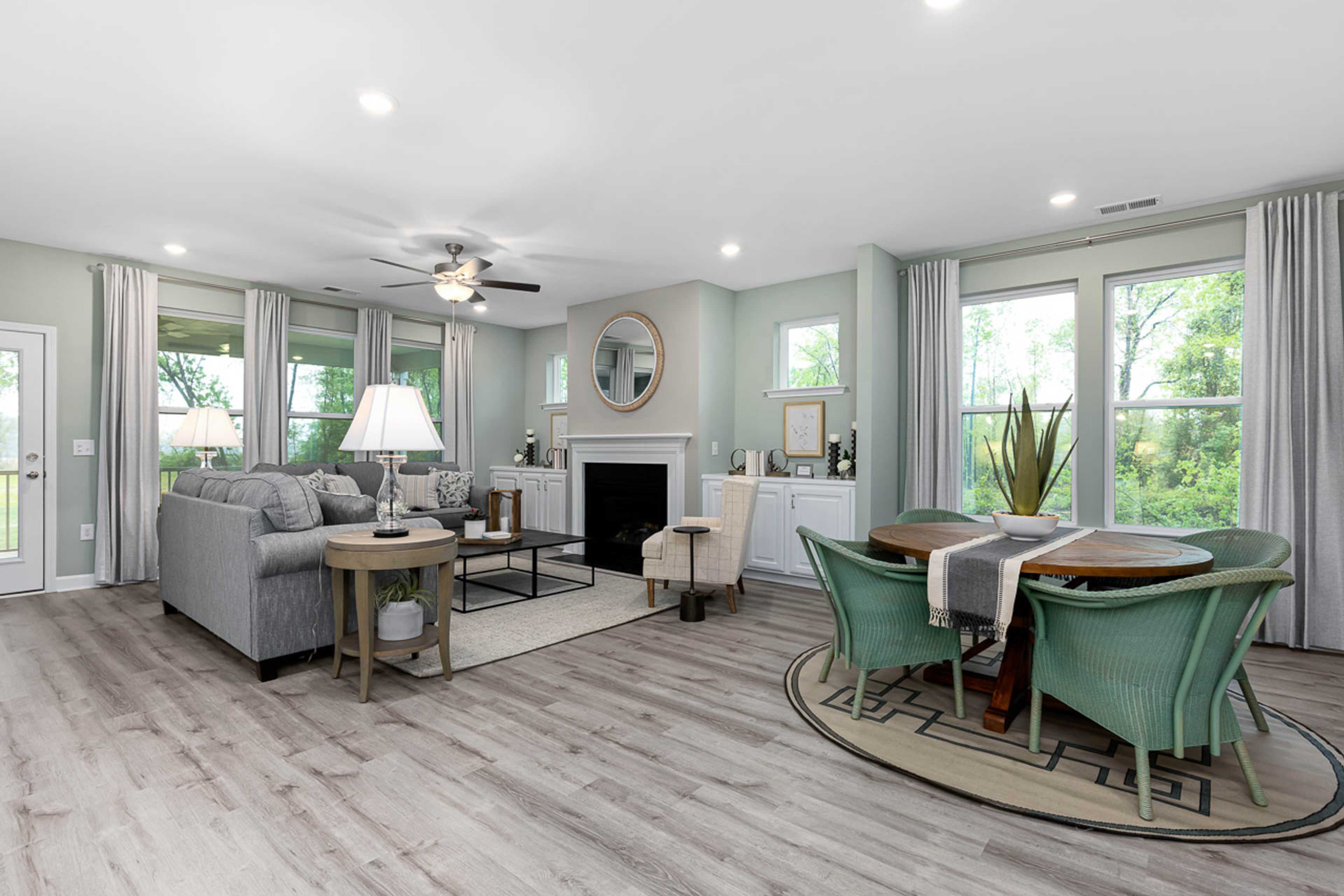 Open-concept living and dining room in Weatherford East, Angier NC featuring hardwood floors, gray sofa, fireplace, and green upholstered chairs