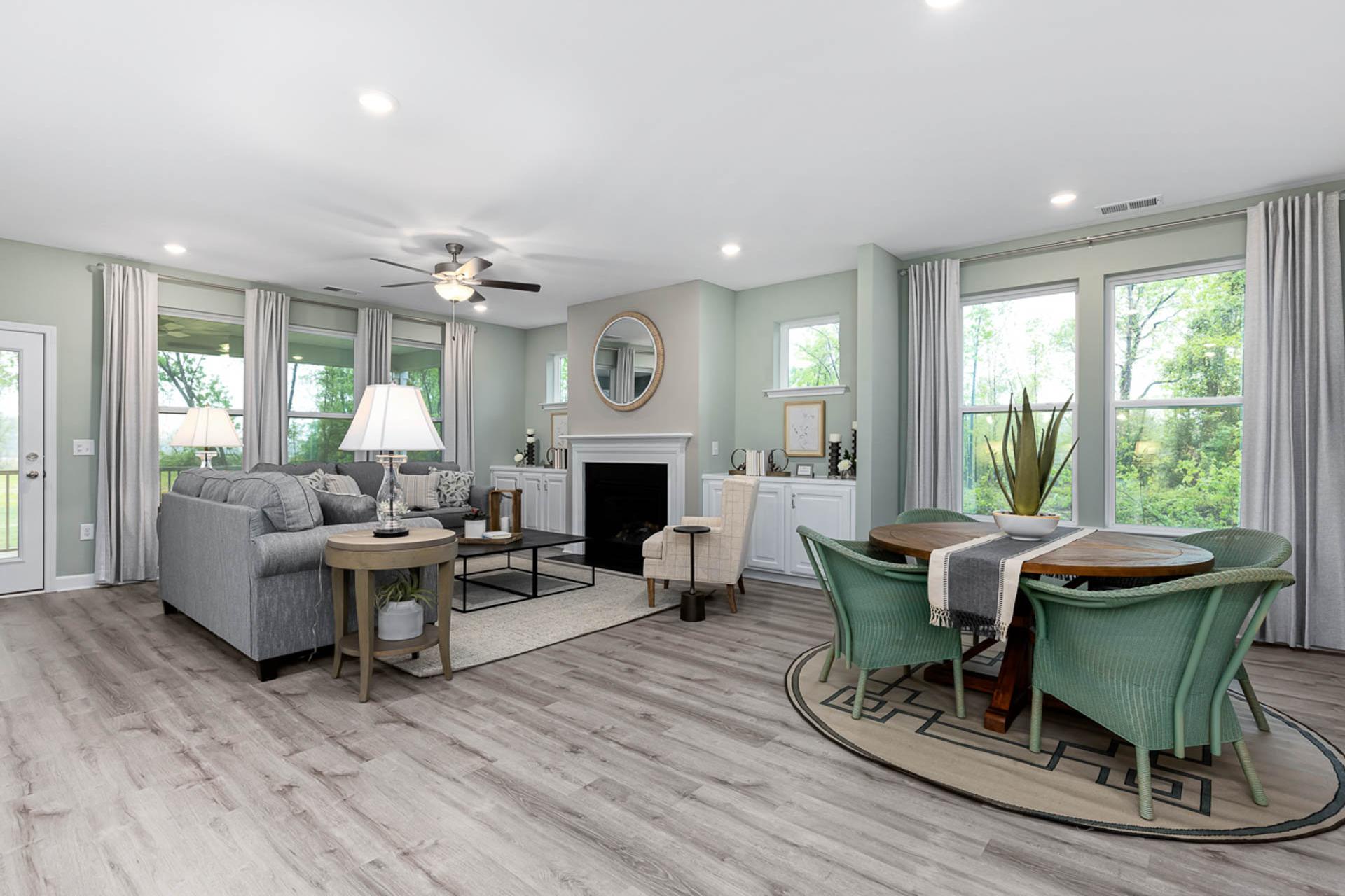 Open-concept living and dining room in Weatherford East, Angier NC featuring hardwood floors, gray sofa, fireplace, and green upholstered chairs