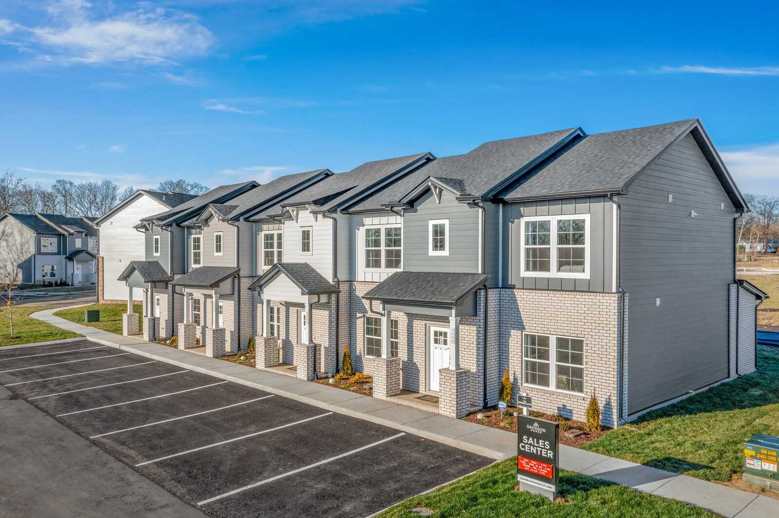 Row of modern 2-story townhomes with gray siding, brick accents, and sales sign in The Towns at Red River, Gallatin, Tennessee by Davidson Homes