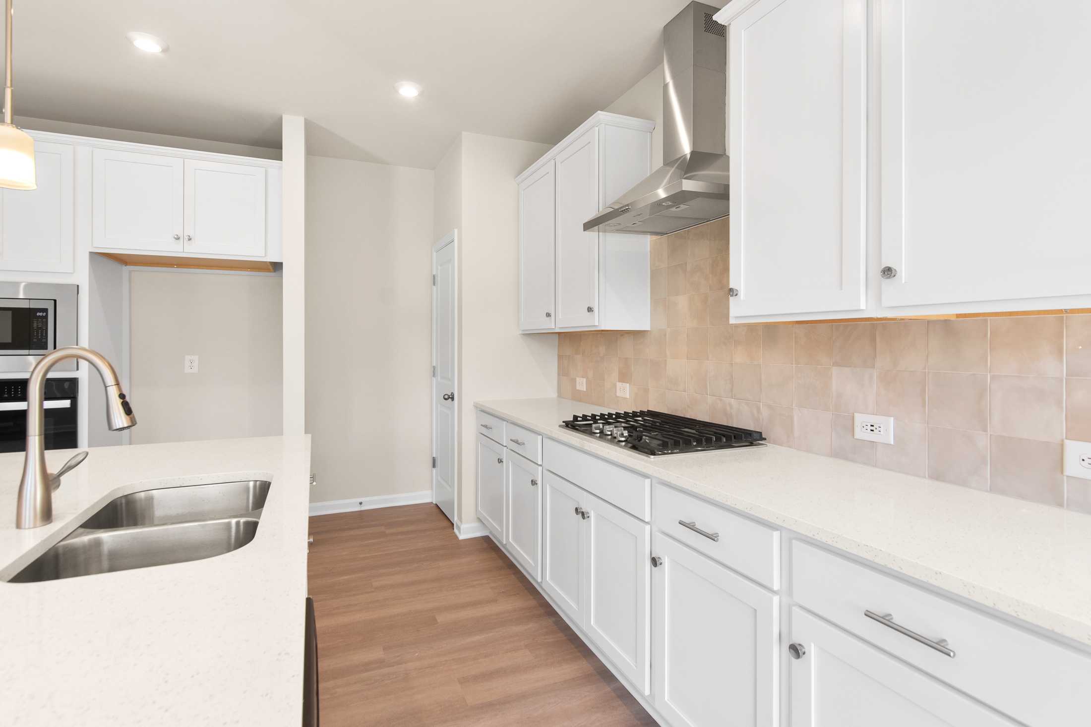 Spacious modern kitchen in The Willow B featuring white shaker cabinets, quartz island with farmhouse sink, and stainless steel gas range