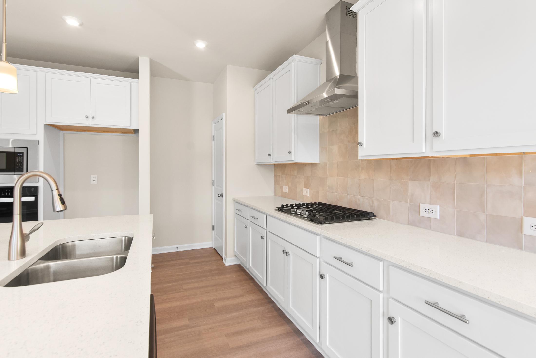 Spacious modern kitchen in The Willow B featuring white shaker cabinets, quartz island with farmhouse sink, and stainless steel gas range