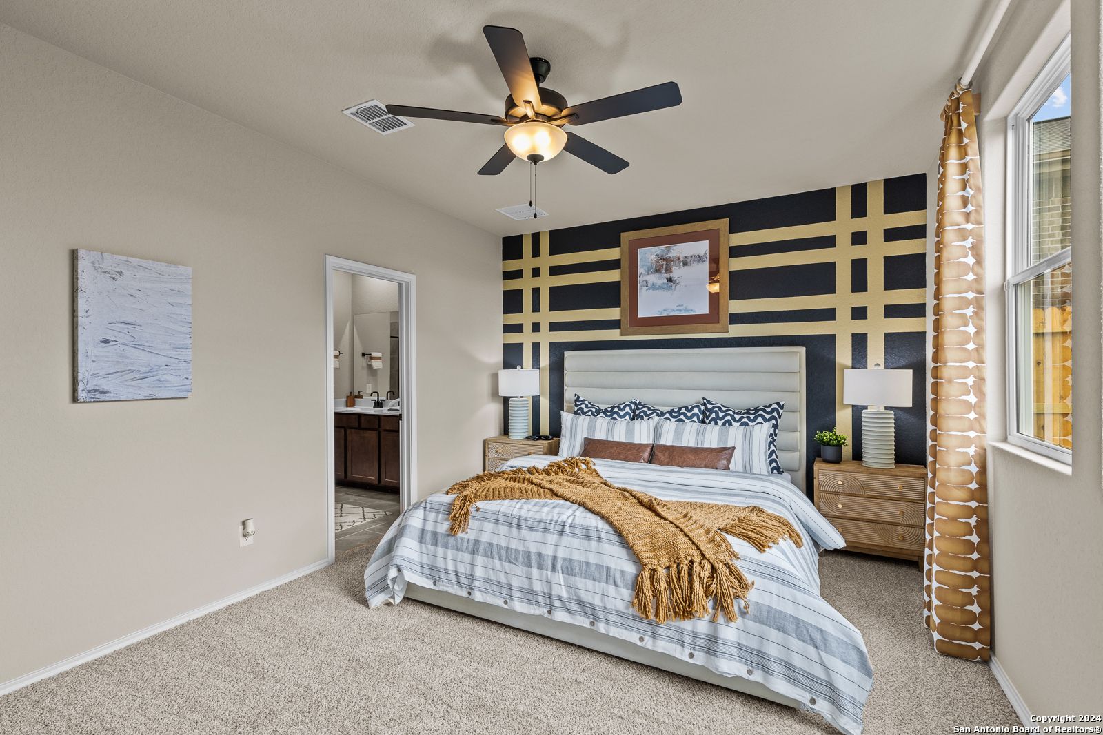 Cozy master bedroom with king bed, striped bedding, black grid accent wall, ceiling fan, and en-suite in Davidson Homes The Douglas F, Bricewood, San Antonio