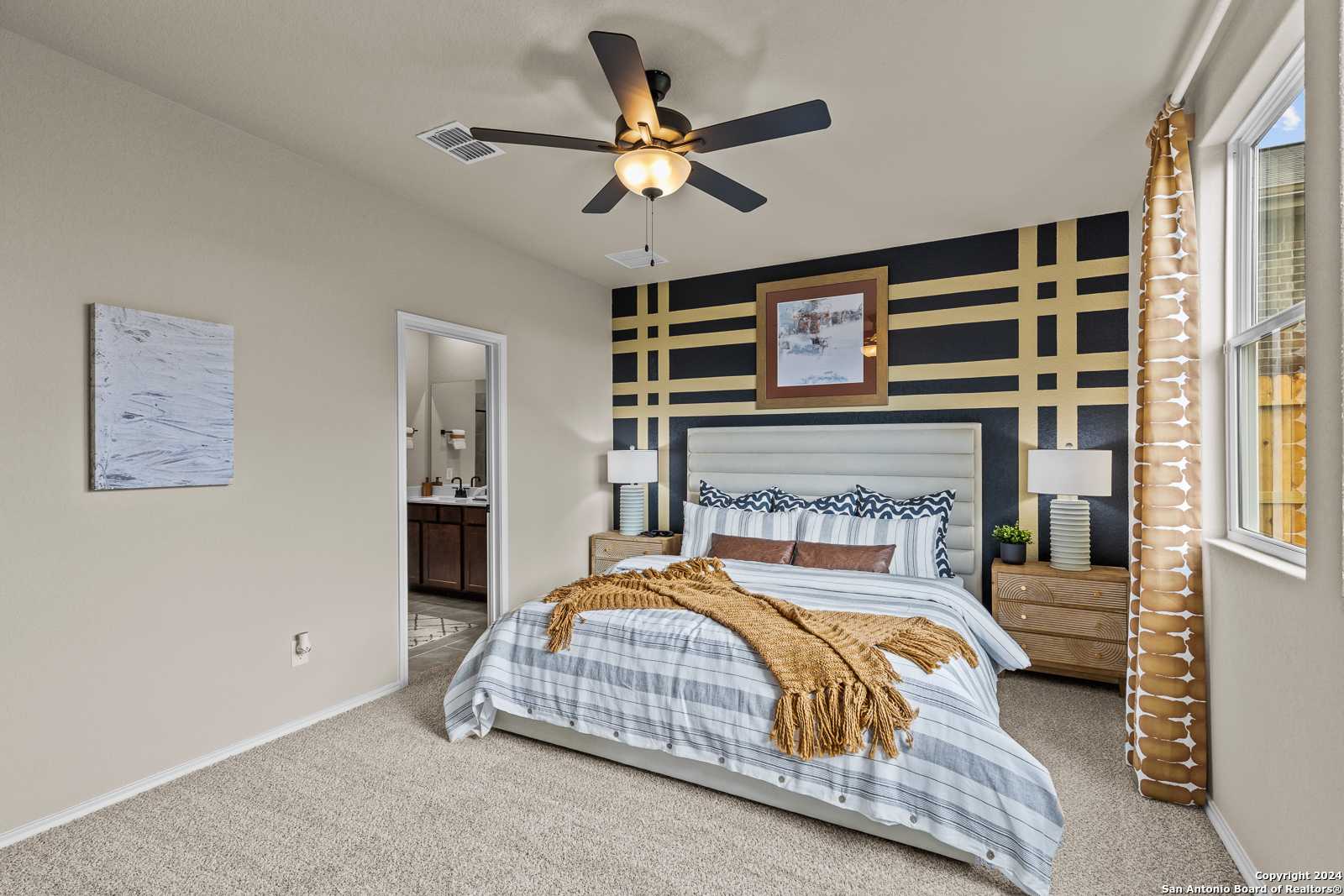 Cozy master bedroom with king bed, striped bedding, black grid accent wall, ceiling fan, and en-suite in Davidson Homes The Douglas F, Bricewood, San Antonio