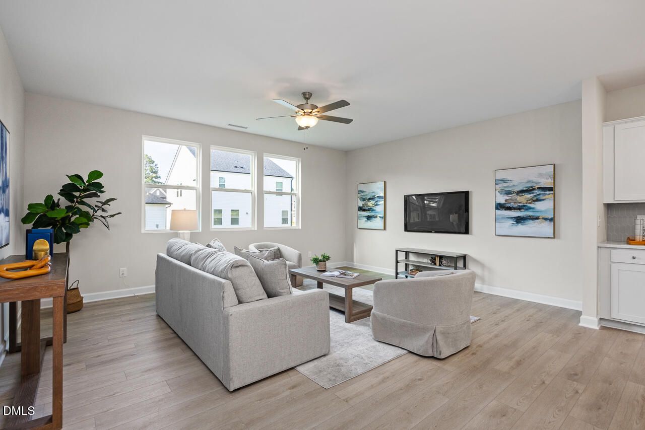 Cozy living room with gray sectional sofa, mounted TV, plants, and large windows in Davidson Homes The Preston A, Lillington, NC