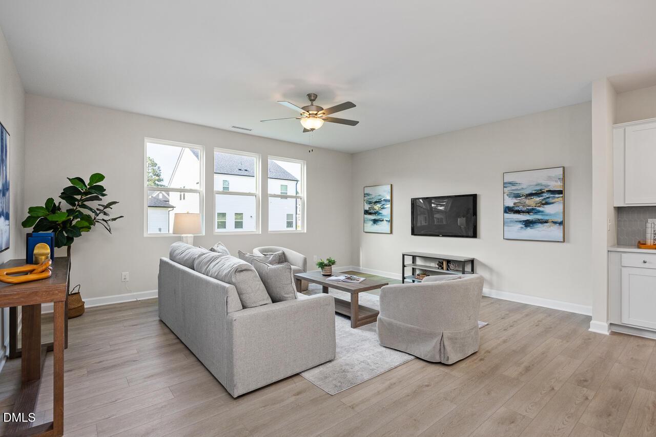 Cozy living room with gray sectional sofa, mounted TV, plants, and large windows in Davidson Homes The Preston A, Lillington, NC