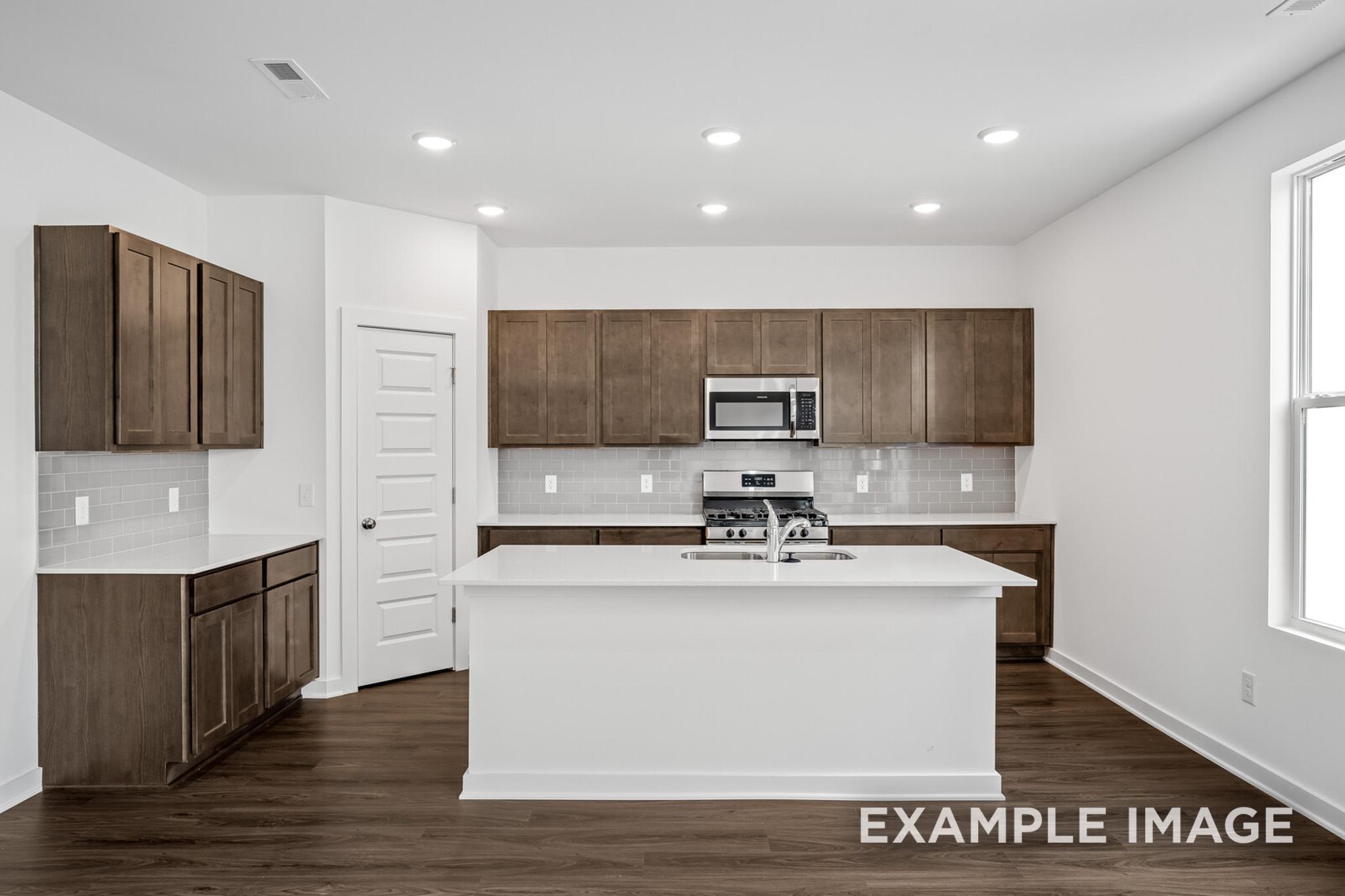 Spacious modern kitchen in The Logan C home with white island, shaker cabinets, stainless appliances, and hardwood floors