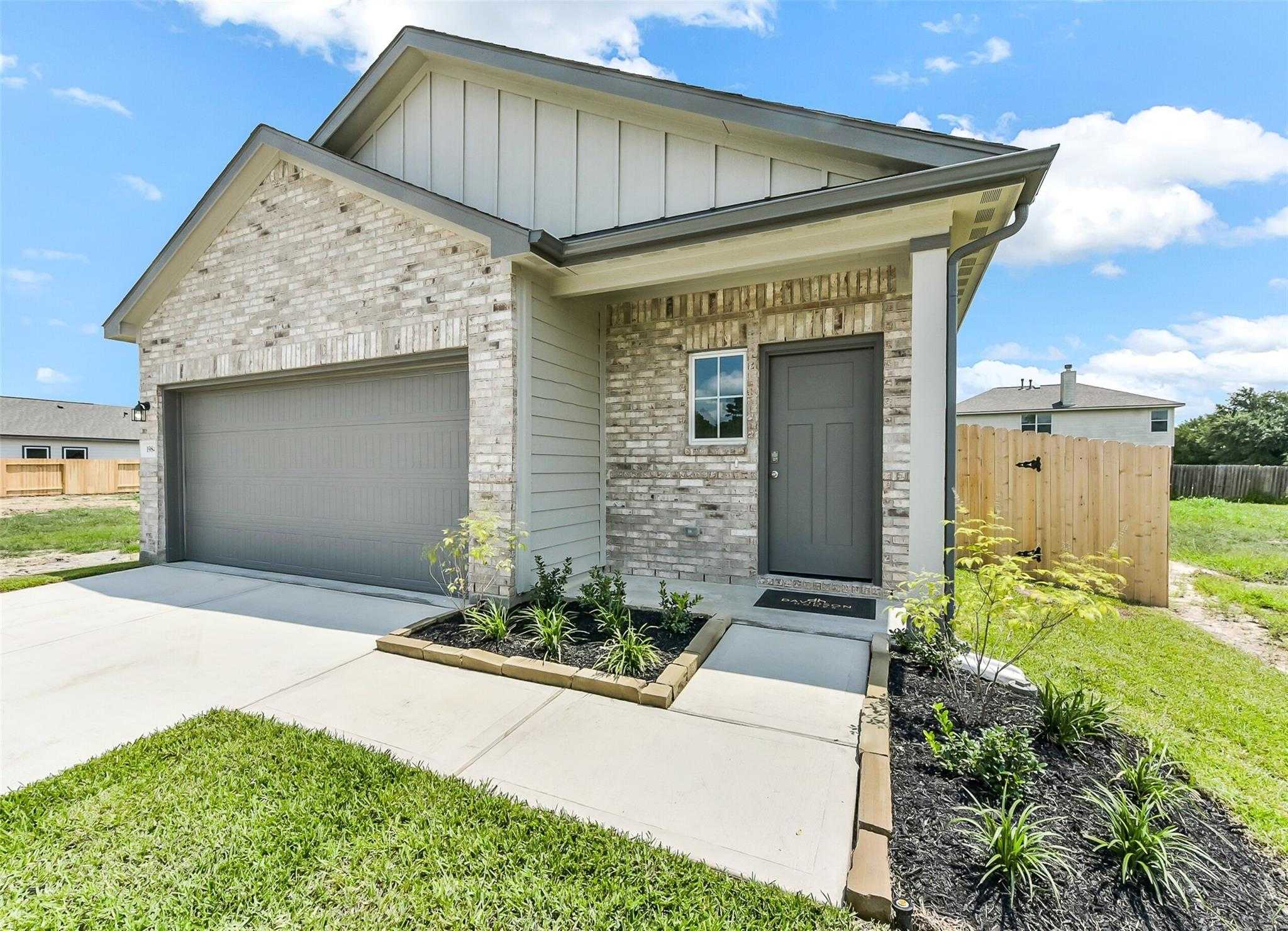 Modern single-story brick home with 2-car garage, gray front door, and landscaped yard in The Villages at WestPointe, Dayton, Texas