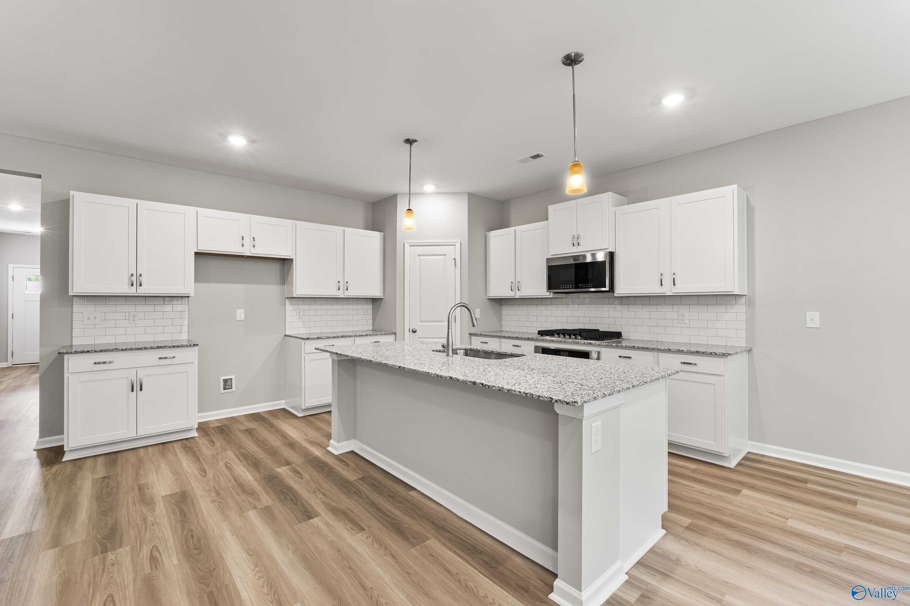 Modern white kitchen with granite island, stainless appliances, subway backsplash in Davidson Homes The Phoenix, Hazel Green, Alabama
