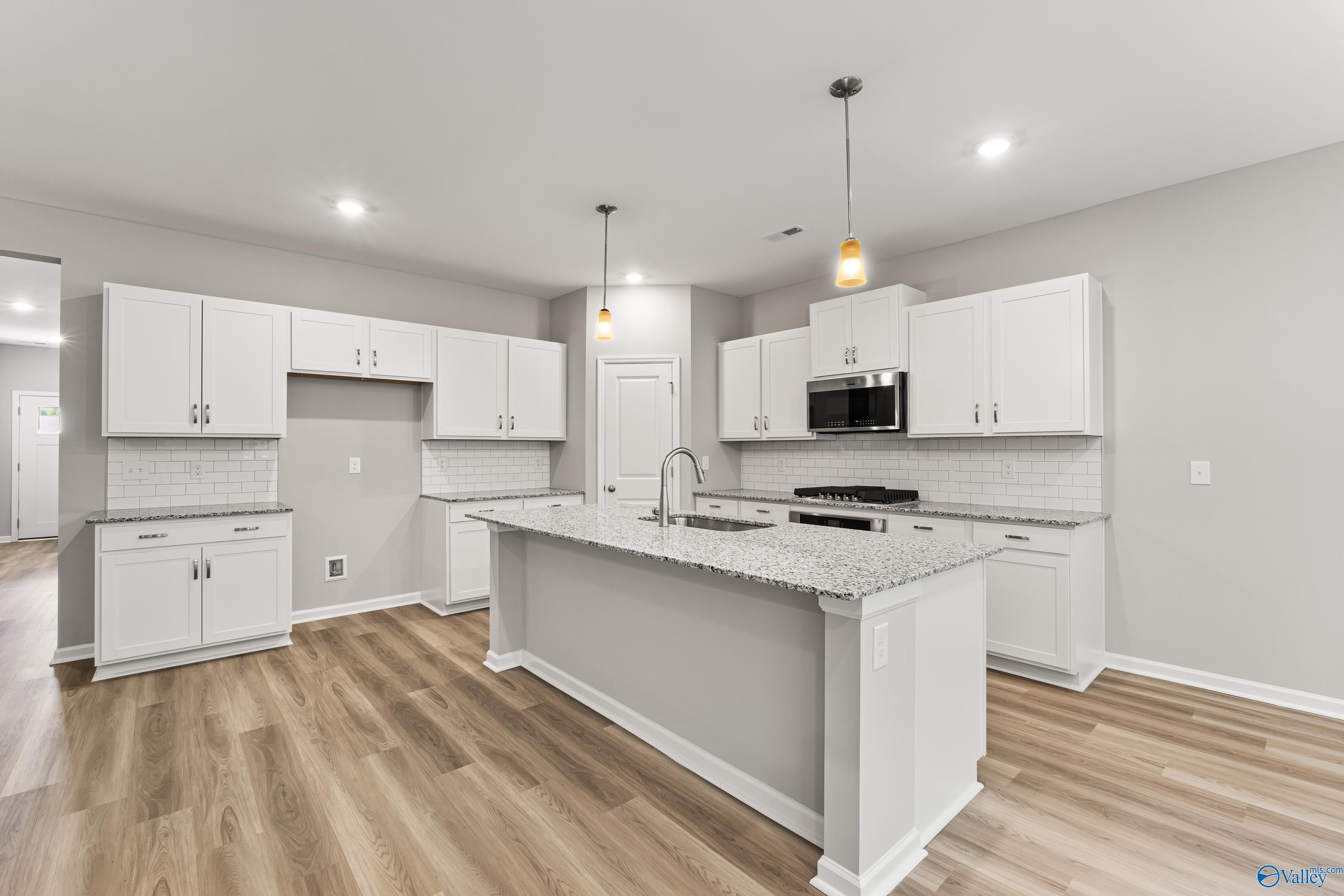 Modern white cabinet kitchen with granite island, subway tile backsplash, stainless appliances in Davidson Homes The Phoenix, Hazel Green, AL