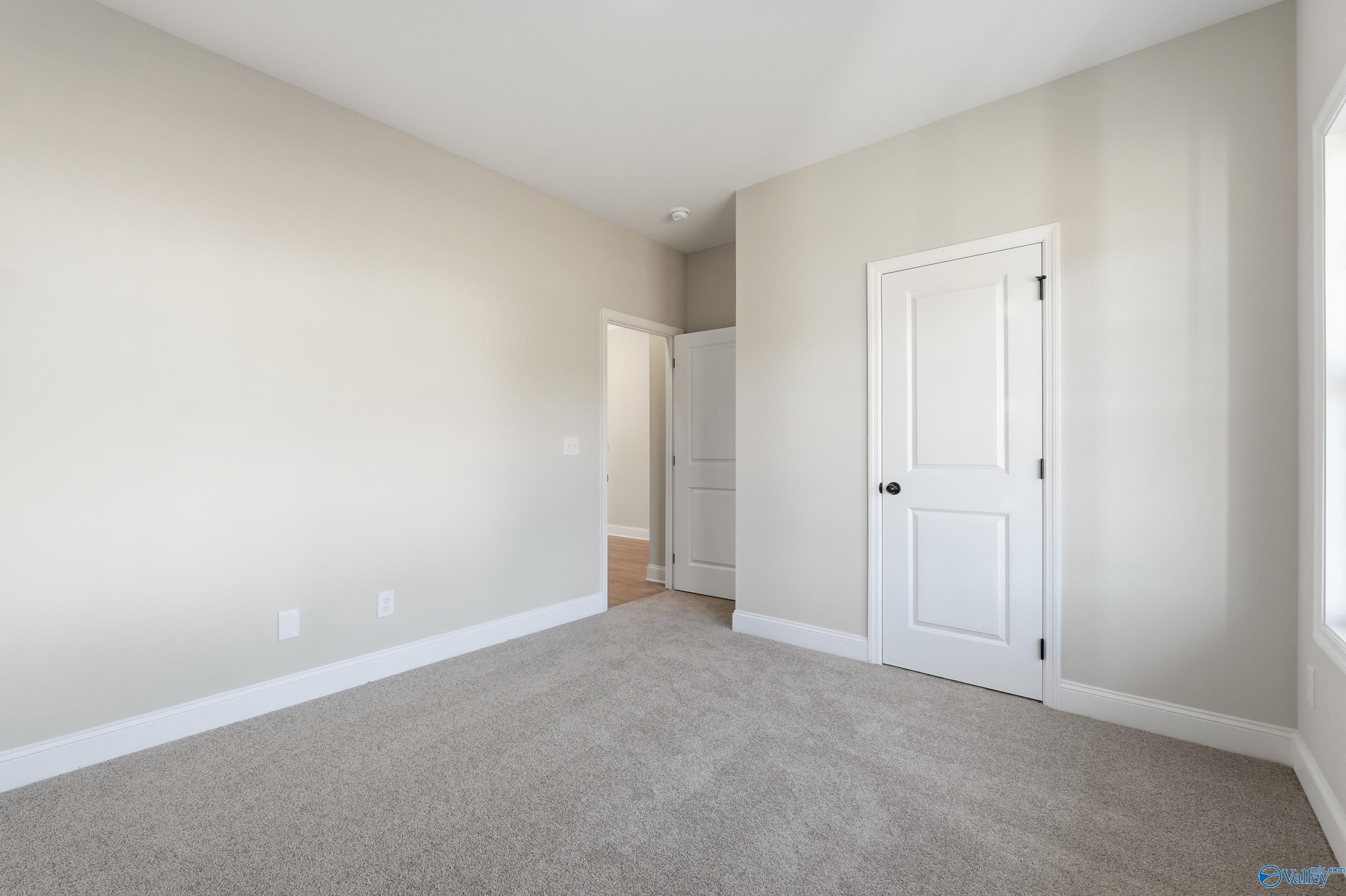Spacious empty bedroom with beige walls, gray carpet, white doors, and large window in Davidson Homes The Franklin E, Hazel Green, Alabama