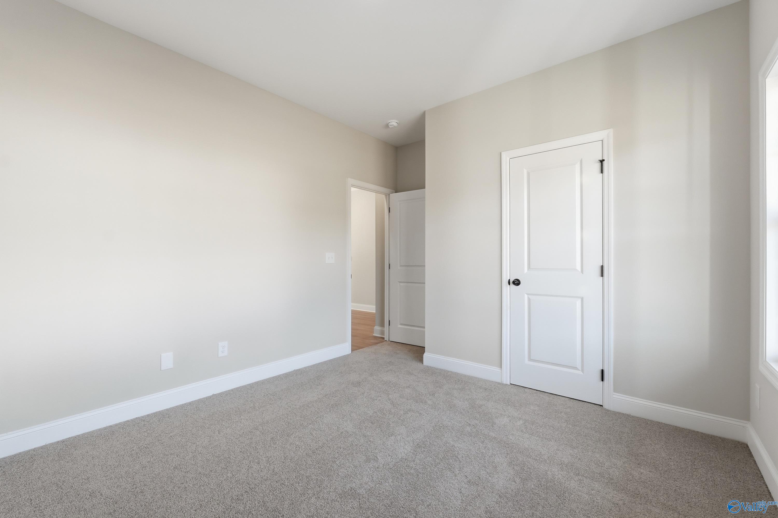 Spacious empty bedroom with beige walls, gray carpet, white doors, and large window in Davidson Homes The Franklin E, Hazel Green, Alabama