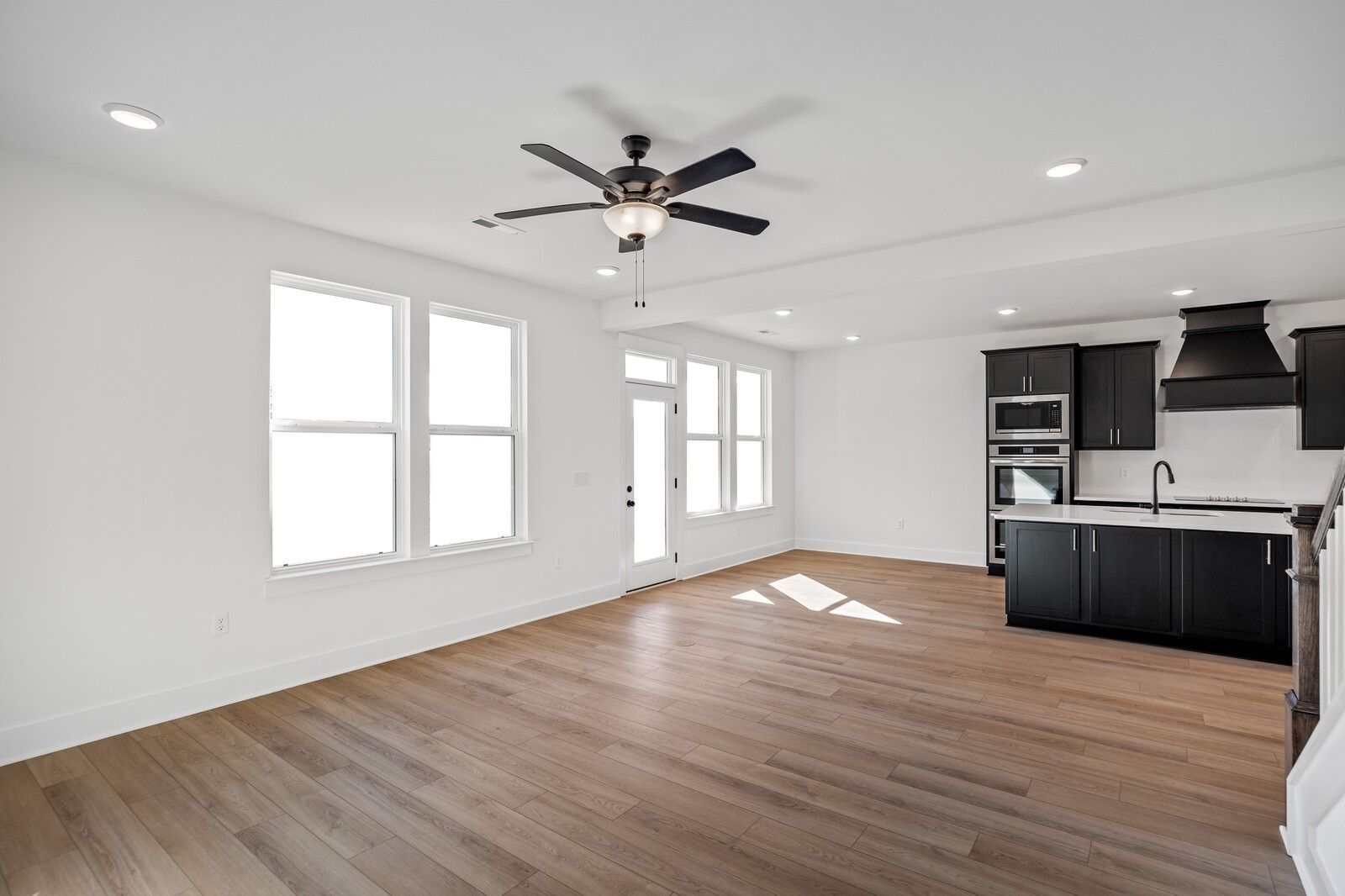 Bright open-concept kitchen-living area with black cabinets, stainless appliances, hardwood floors, and large windows in The Willow C, Gallatin, TN