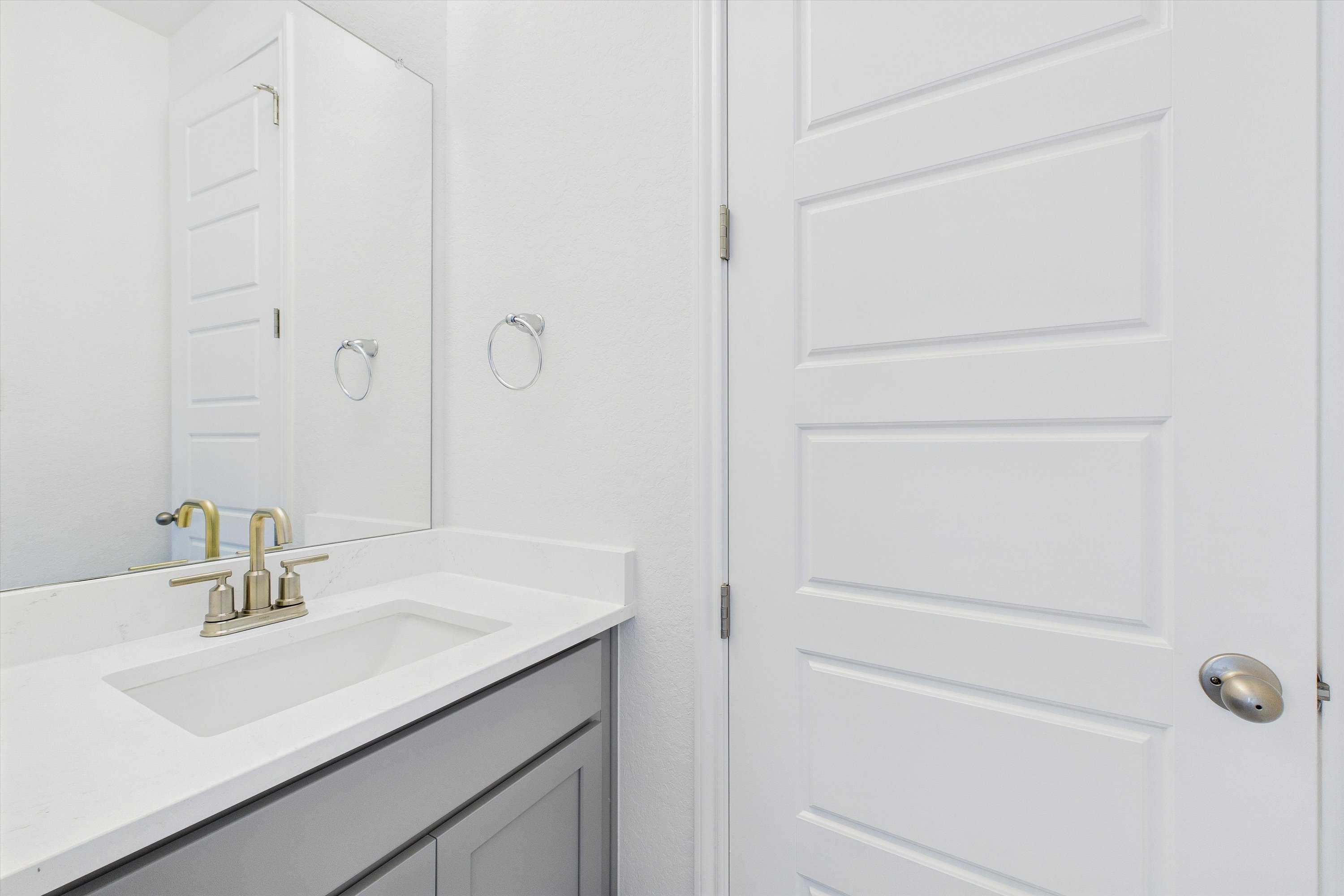 Modern bathroom vanity with gray cabinets, white quartz countertop, gold faucet and mirror in Davidson Homes The Summerlin C, Castroville, Texas