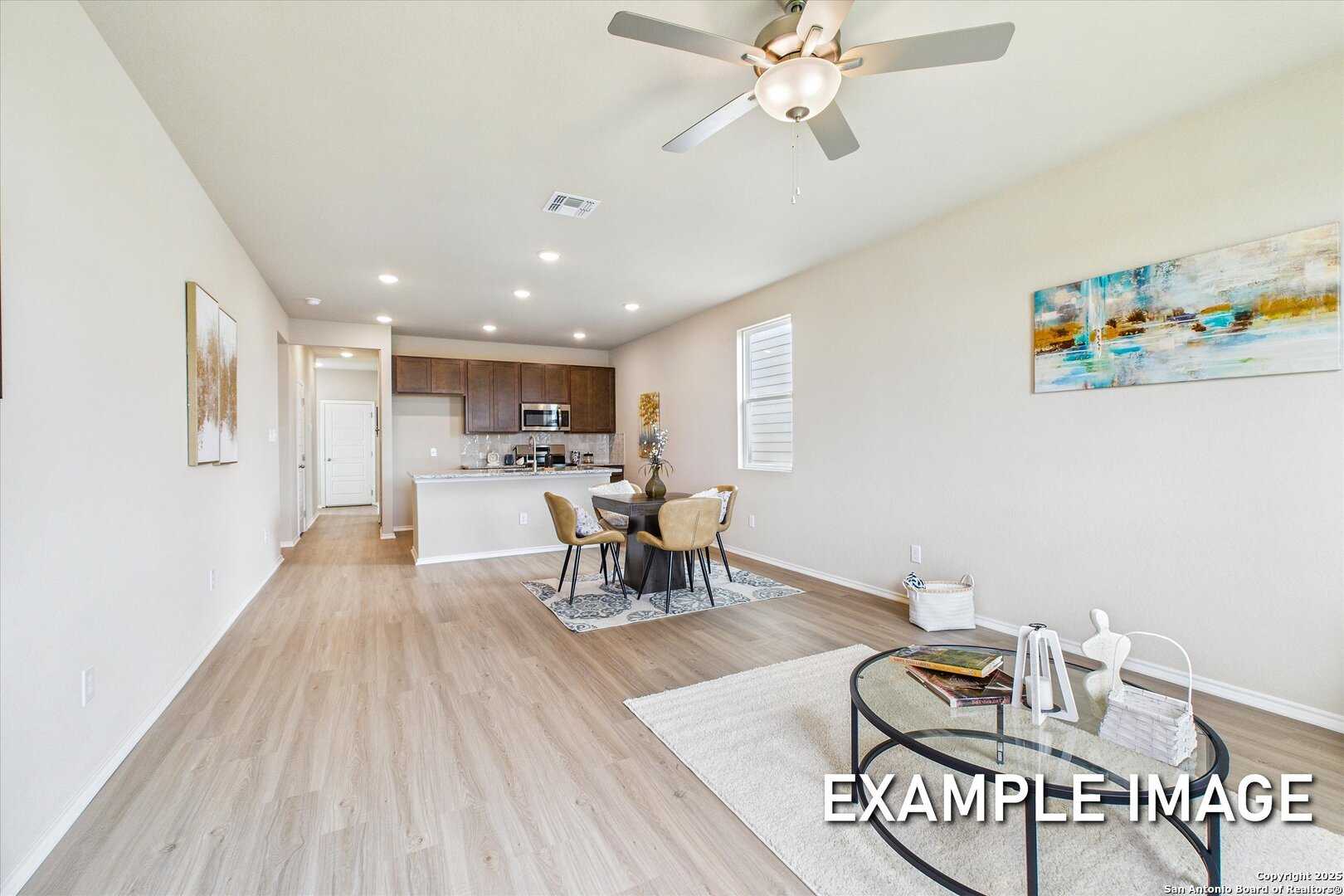 Open-concept dining and living area with light wood floors, ceiling fan, and kitchen cabinets in Davidson Homes The Comal B, San Antonio