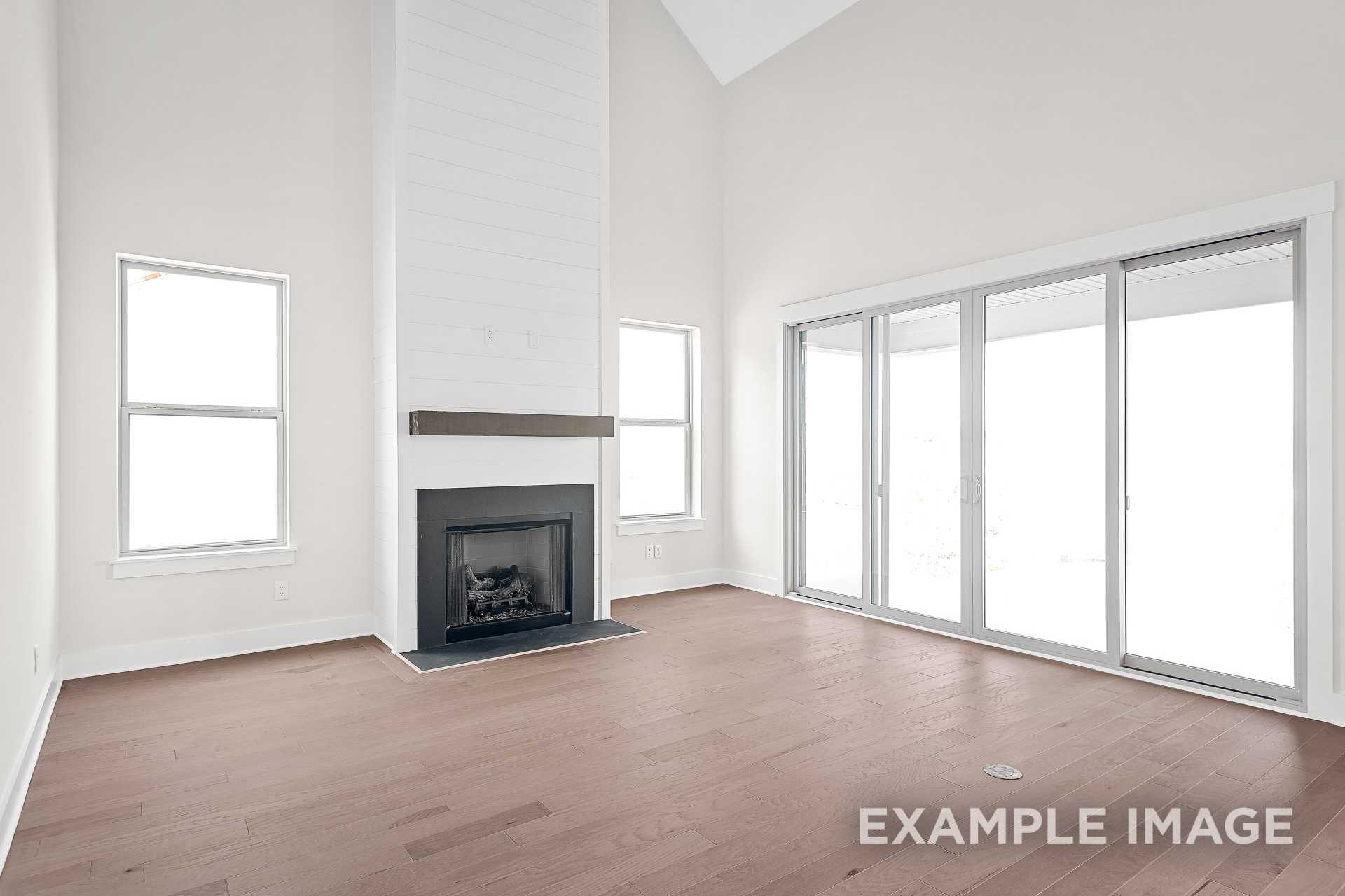 Spacious great room in The Hawkins with tall white brick fireplace, hardwood floors, and large sliding glass doors