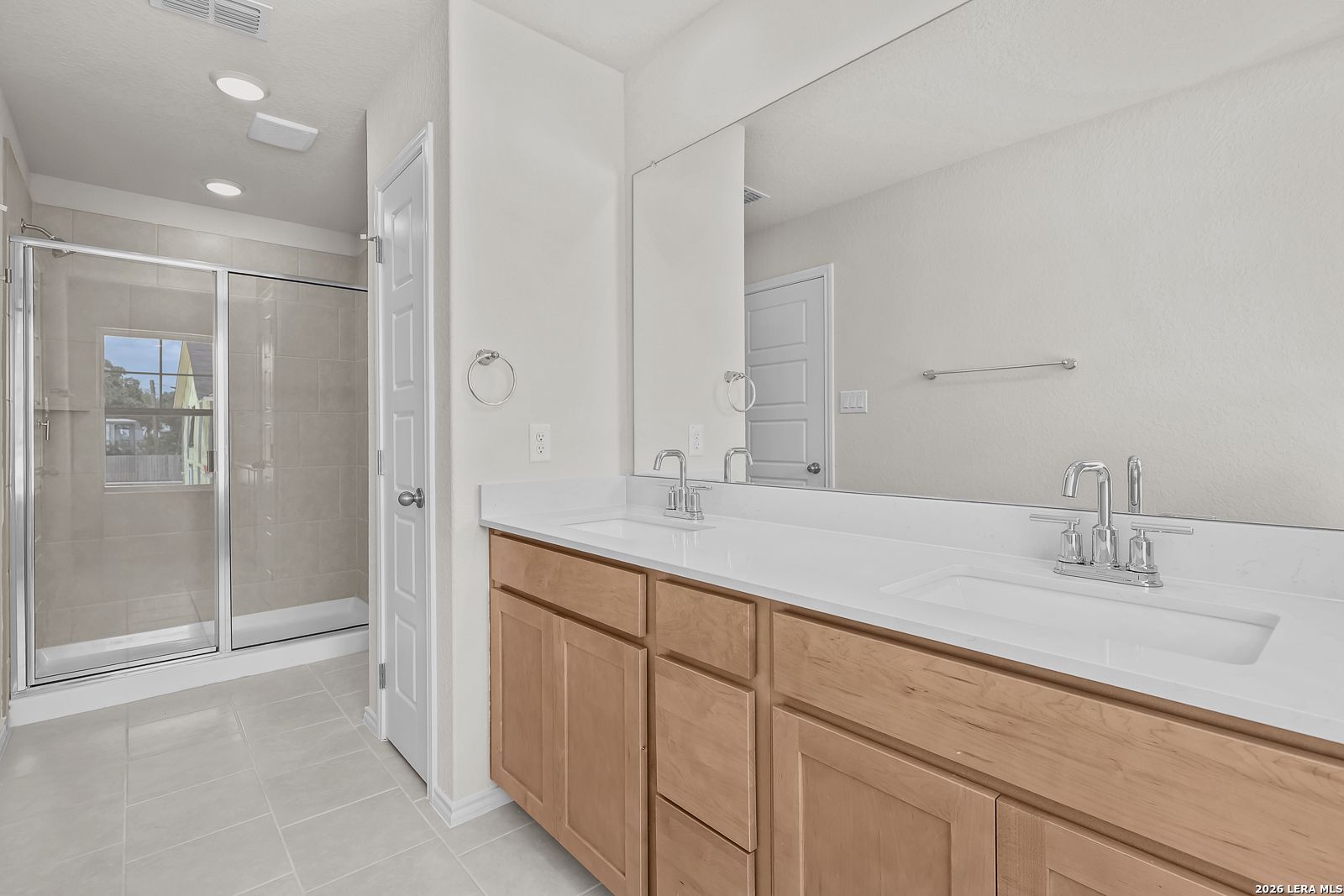 Modern bathroom with double vanity, quartz countertops, and glass-enclosed shower in The Gillian B home, San Antonio.