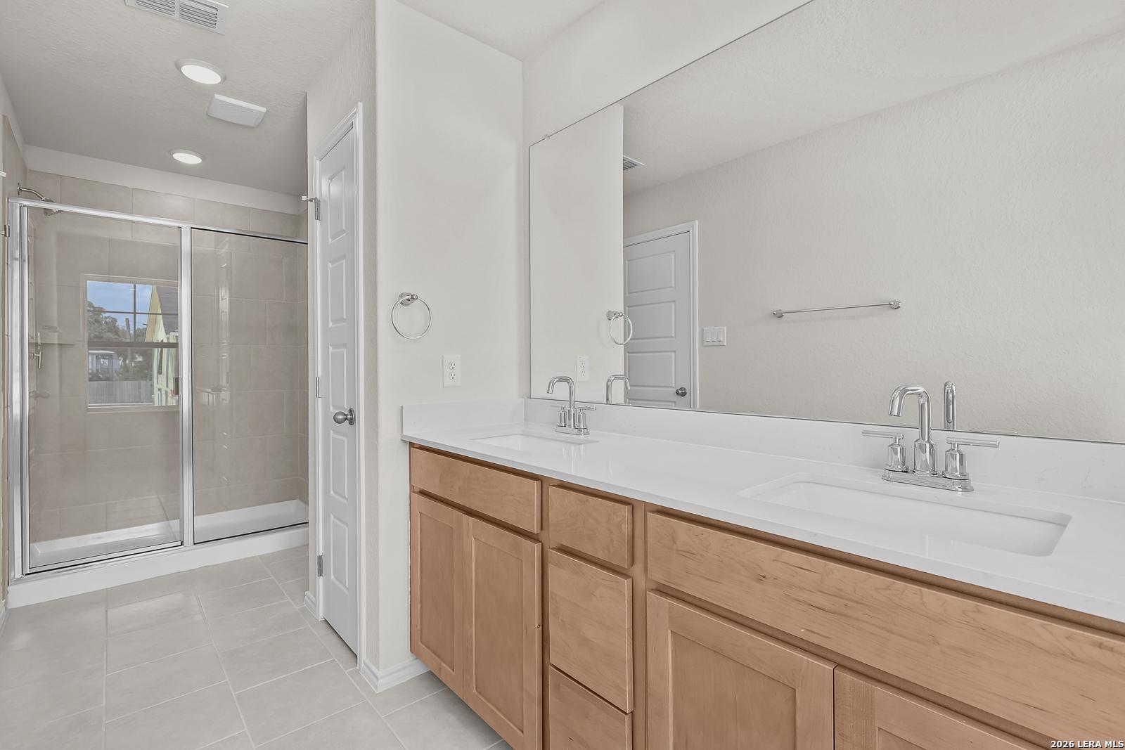 Modern bathroom with double vanity, quartz countertops, and glass-enclosed shower in The Gillian B home, San Antonio.