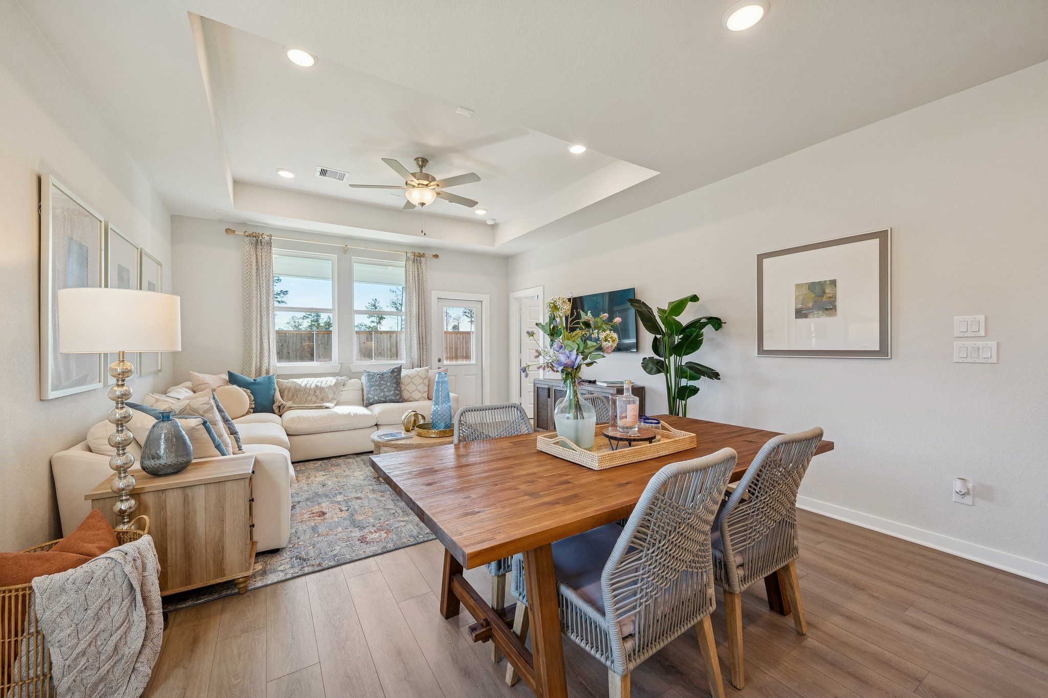 Spacious open-concept living and dining area in Spring Branch Crossing Conroe Texas with hardwood floors, beige sofa, wooden table, and rattan chairs