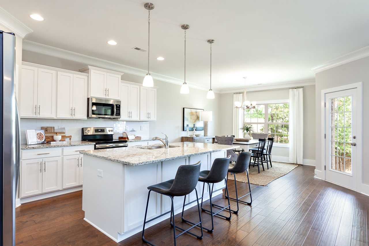 Spacious The Rockford kitchen by Davidson Homes featuring white cabinets, granite island with bar stools, stainless appliances, and open dining area on hardwood floors