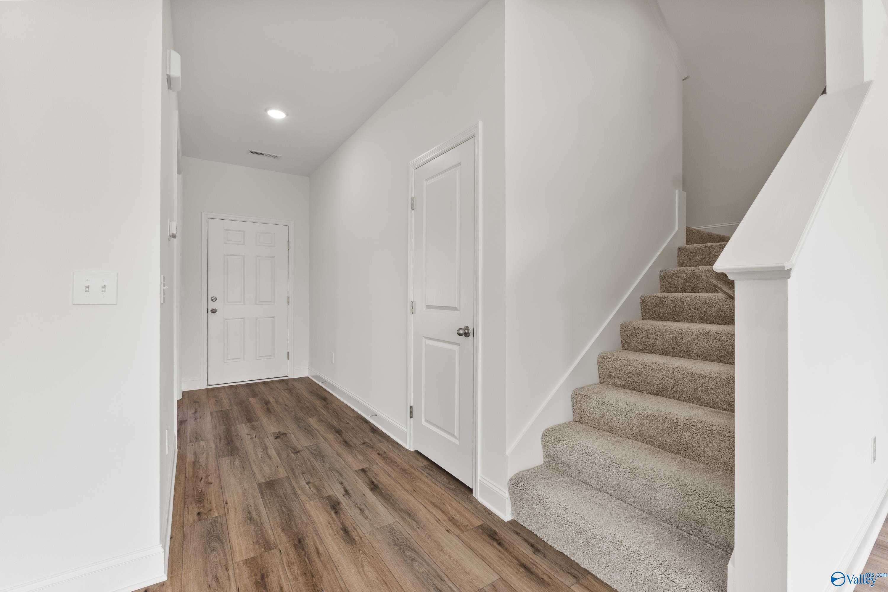 Bright hallway with hardwood floors, white walls, and carpeted staircase in Davidson Homes The Shelby A, New Market, Alabama