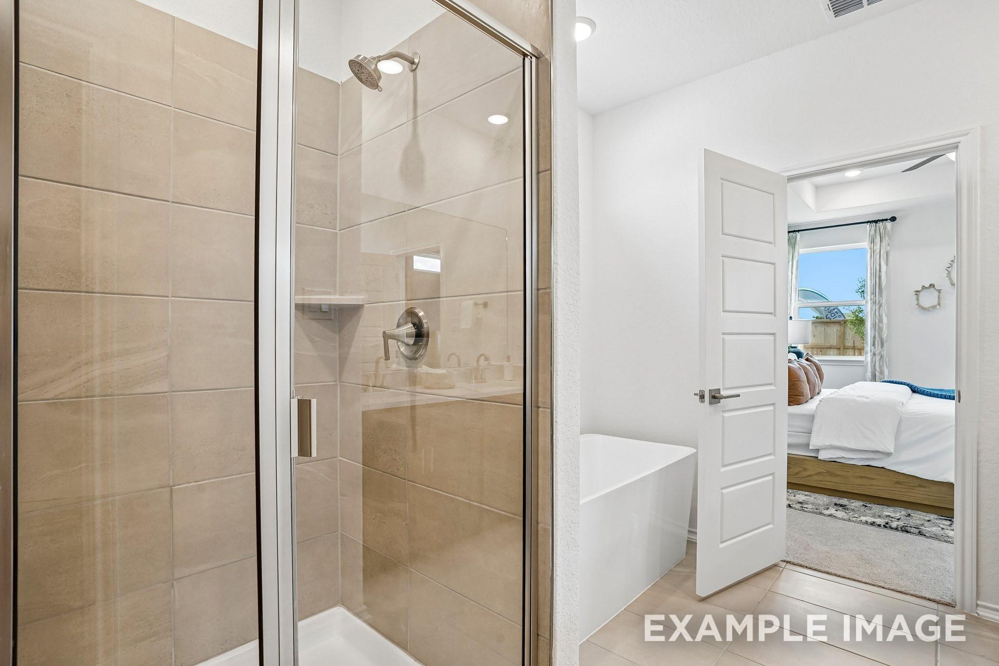 Glass walk-in shower and freestanding tub in primary bath with view of bedroom in Davidson Homes Ashport J, Crosby, TX