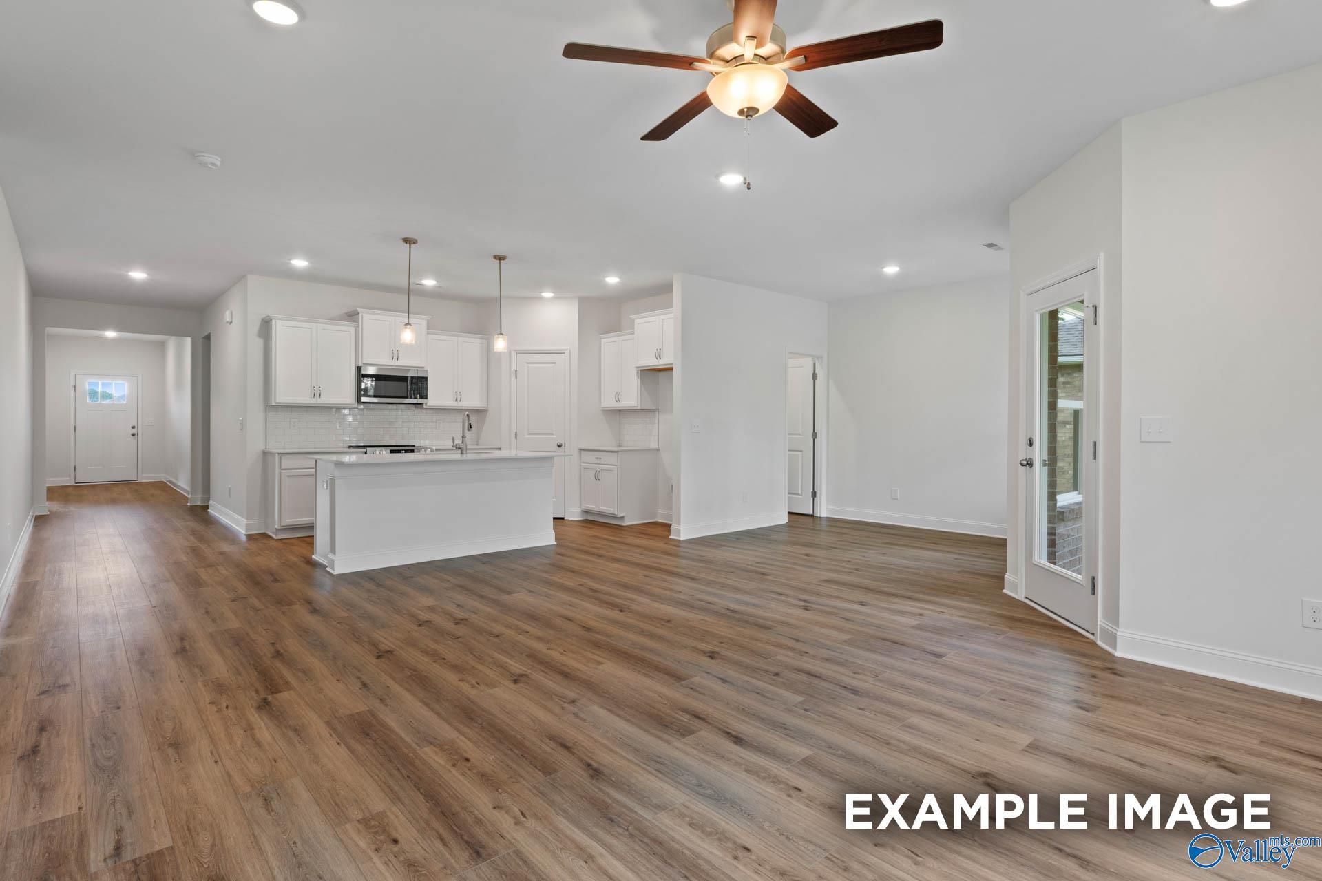 Open-concept kitchen and living area with white cabinets, island, hardwood floors, and ceiling fan in The Daphne E by Evermore Homes, Harvest, AL