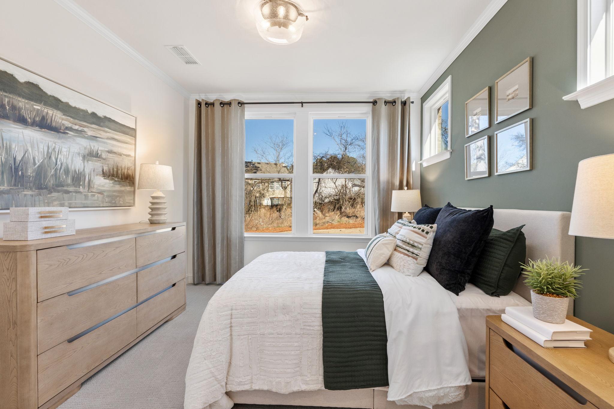 Spacious primary bedroom in Fern Hollow Buford GA by Davidson Homes with sage green walls neutral bedding large landscape art and wood furniture