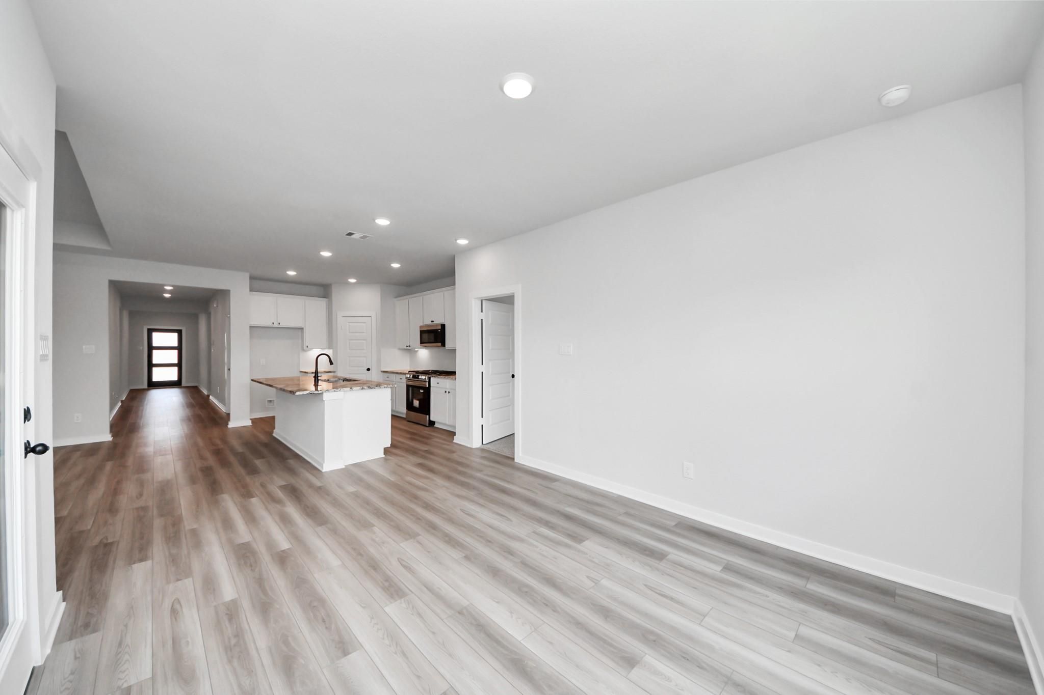 Open-concept kitchen and living area with wood-look flooring in The Everett C floor plan at River Ranch Meadows, Dayton, TX.