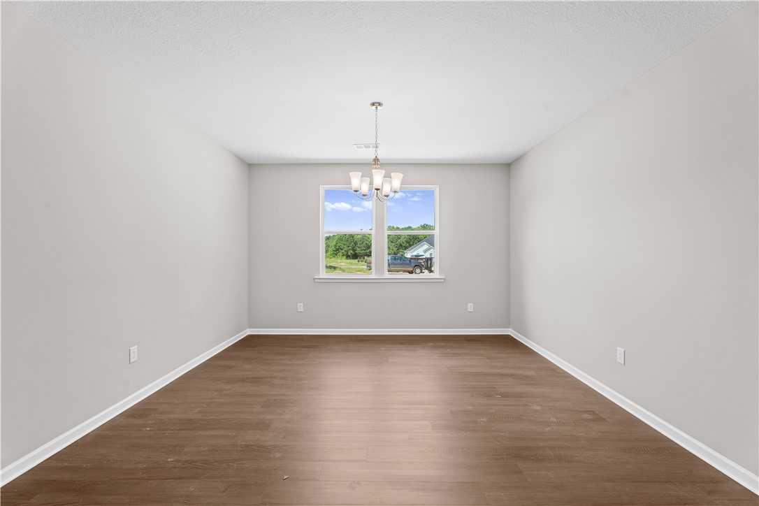 Bright empty living room with hardwood floors, gray walls, large window overlooking trees, chandelier in The Orion 4-bedroom home, Cusseta, Alabama