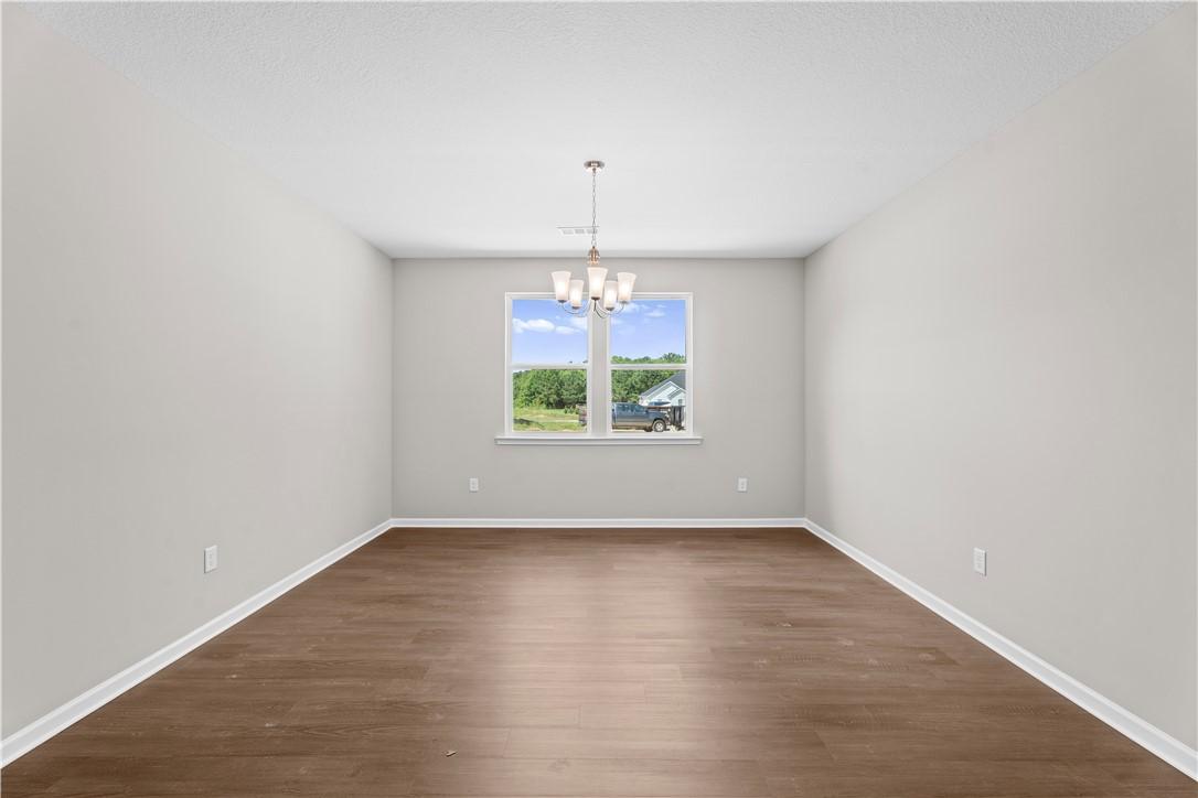Spacious empty room with hardwood floors, gray walls, chandelier, and large window view in Evermore Homes The Orion, Cusseta, Alabama