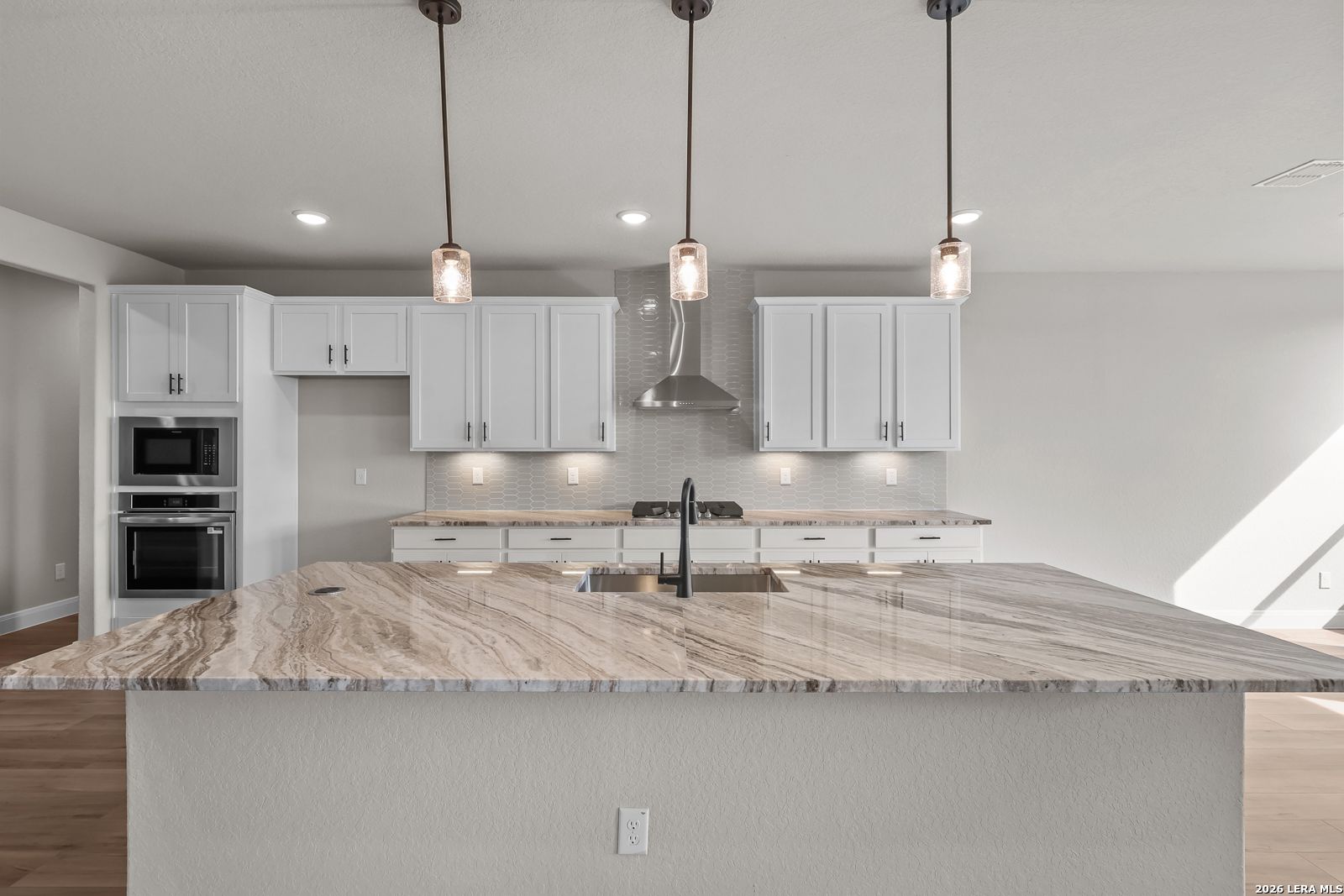 Kitchen island with marble countertops, pendant lights, and white cabinetry in Davidson Homes The Foster E, Potranco Oaks, Castroville, TX