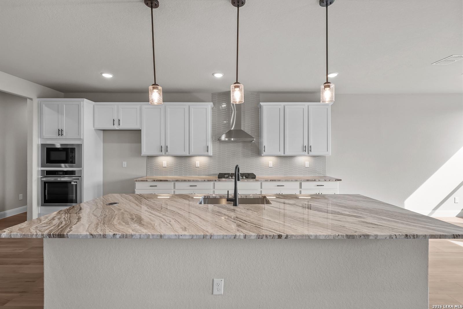 Kitchen island with marble countertops, pendant lights, and white cabinetry in Davidson Homes The Foster E, Potranco Oaks, Castroville, TX