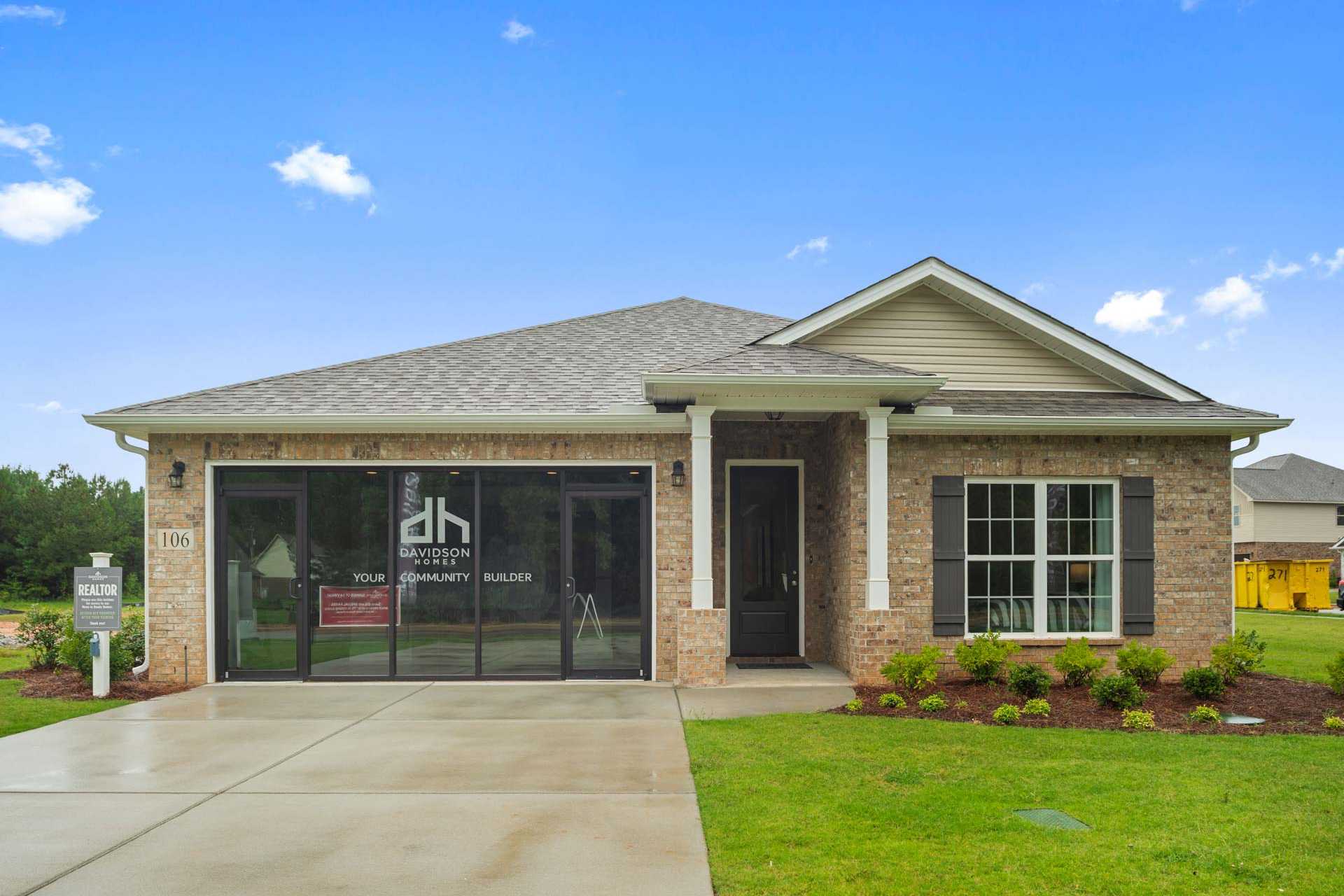New brick home exterior at Durham Farms in Harvest, Alabama by Davidson Homes with covered porch, garage, and lush landscaping