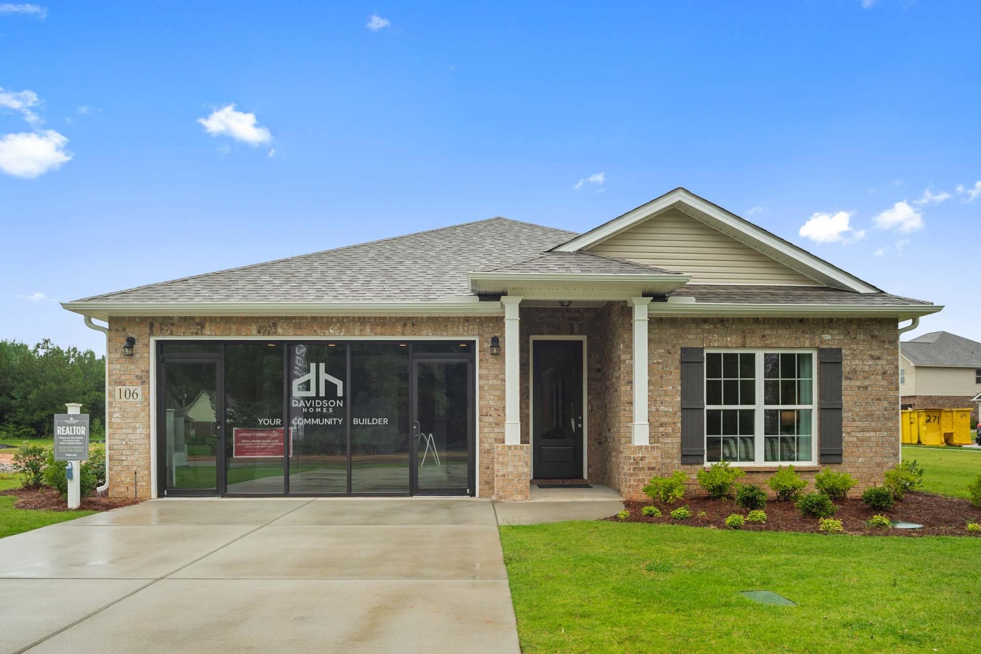 New brick home exterior at Durham Farms in Harvest, Alabama by Davidson Homes with covered porch, garage, and lush landscaping