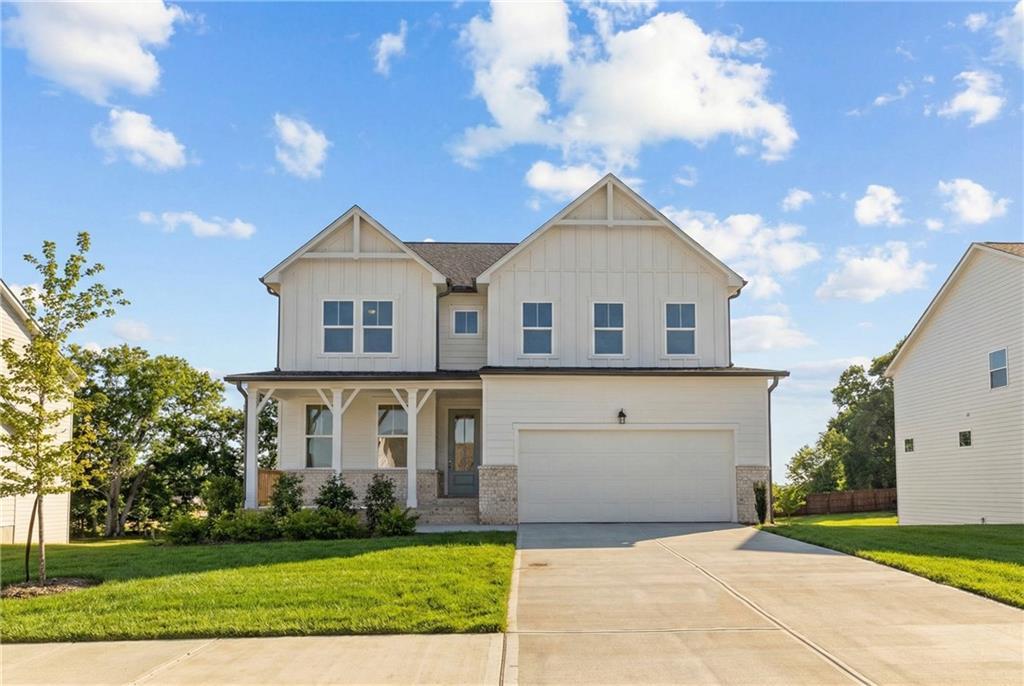 Charming white board-and-batten 3-story home with 2-car garage, covered porch, and lush green lawn in Wehunt Meadows, Hoschton, Georgia