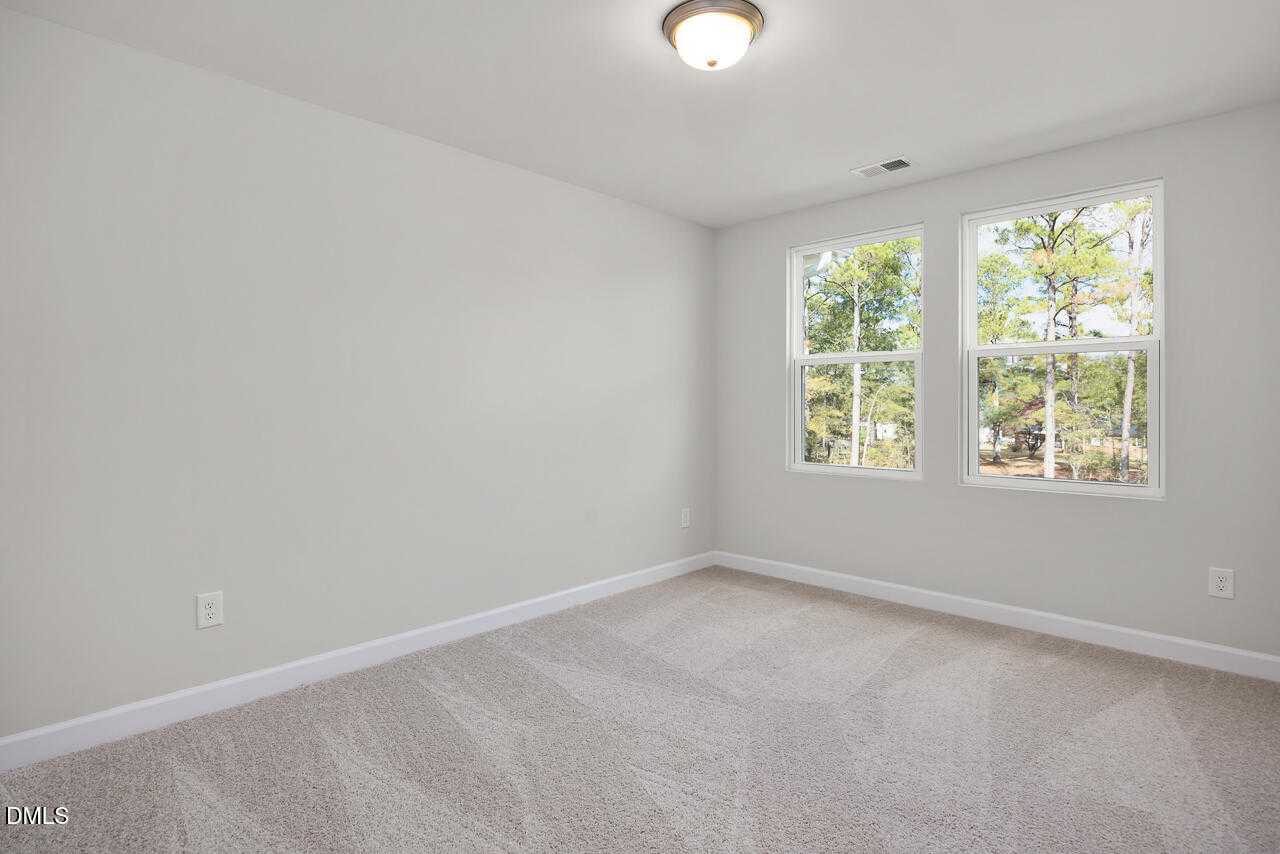 Bright bedroom with large windows overlooking wooded backyard, light gray walls, and neutral carpet in Davidson Homes The Warren plan, Fuquay-Varina, NC