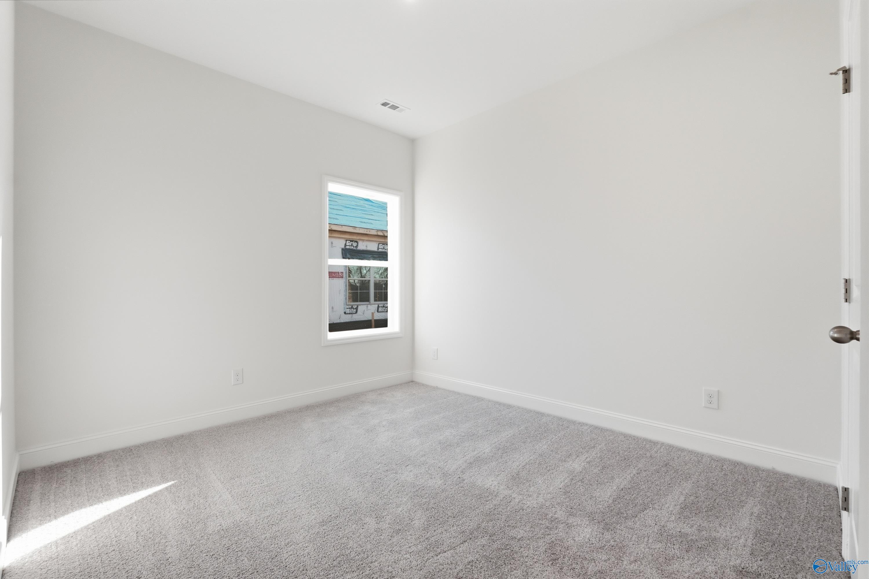 Bright empty bedroom with white walls, gray carpet, and large window in Davidson Homes The Asheville C, Meridianville, Alabama