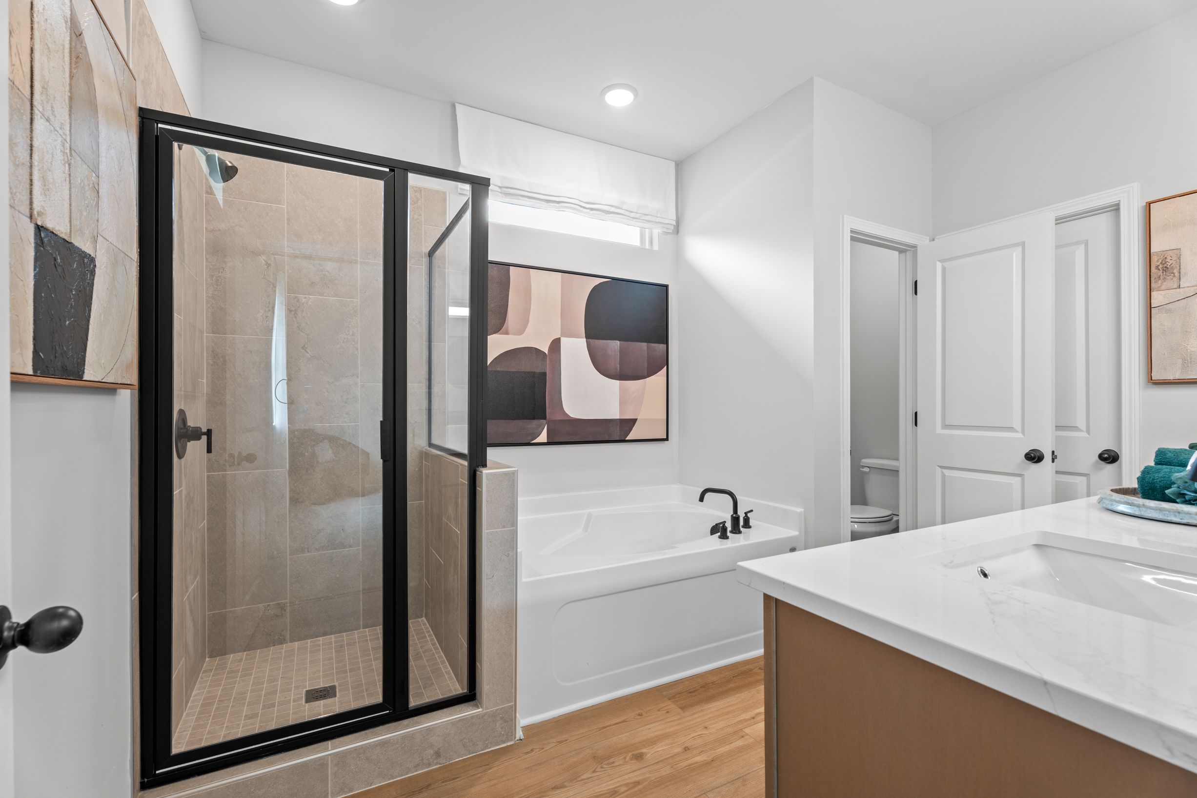 Modern primary bathroom at Links Crossing in Auburn, AL featuring a walk-in glass shower, soaking tub, and vanity.