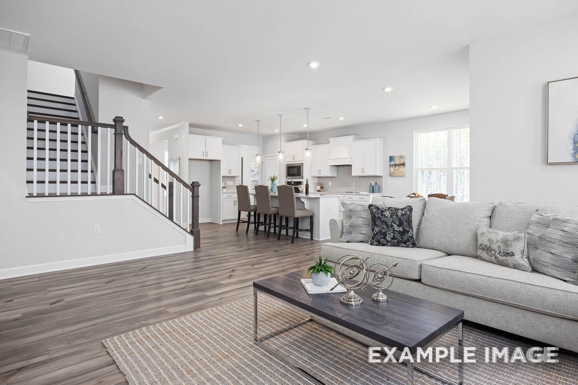 Spacious open-concept kitchen and living room in The Ash two-story home with white island, gray sofa, and modern staircase