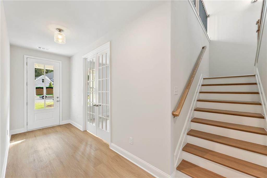 Bright entry foyer with light oak hardwood floors, glass-paneled front door, and grand wooden staircase in Davidson Homes The Hampton C, Buford, GA