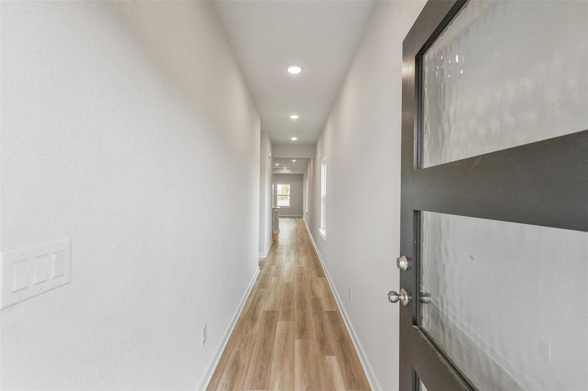Bright hallway with light oak floors, white walls, recessed lighting, and frosted glass front door in Davidson Homes The Colorado G, Magnolia, Texas